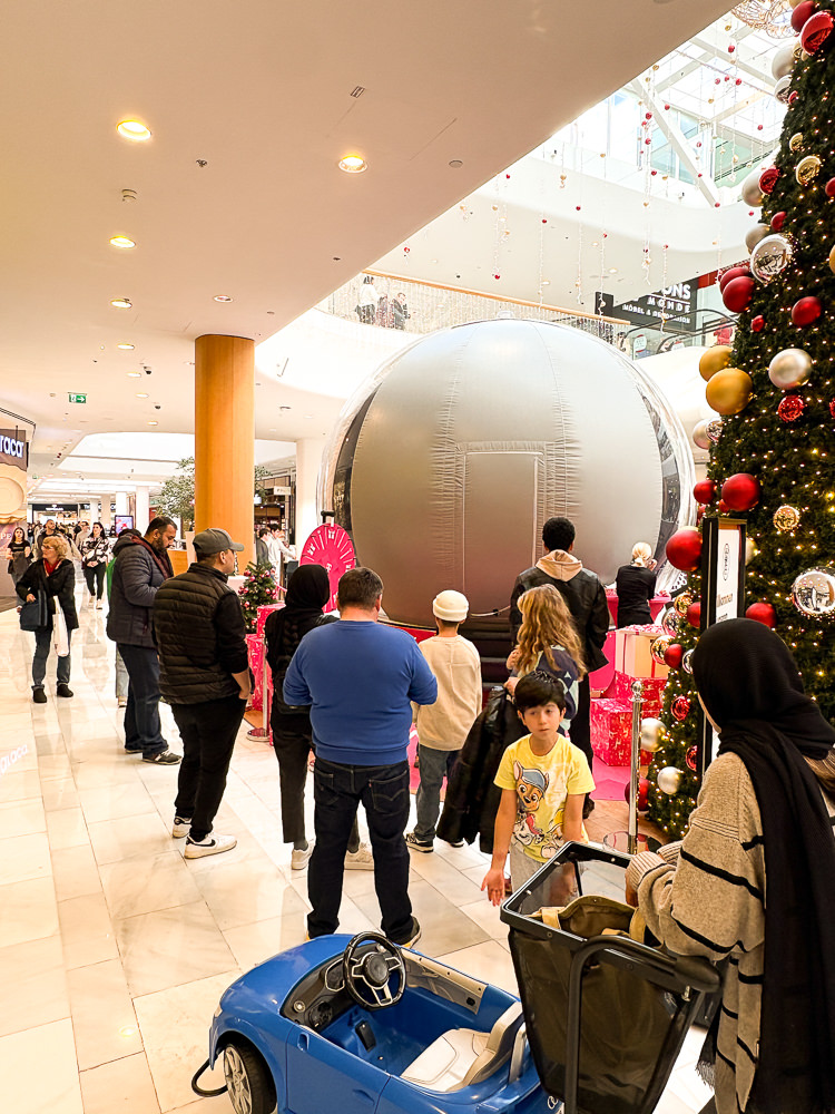 Besucher warten vor der Schneekugel-Fotoaktion in der Mall