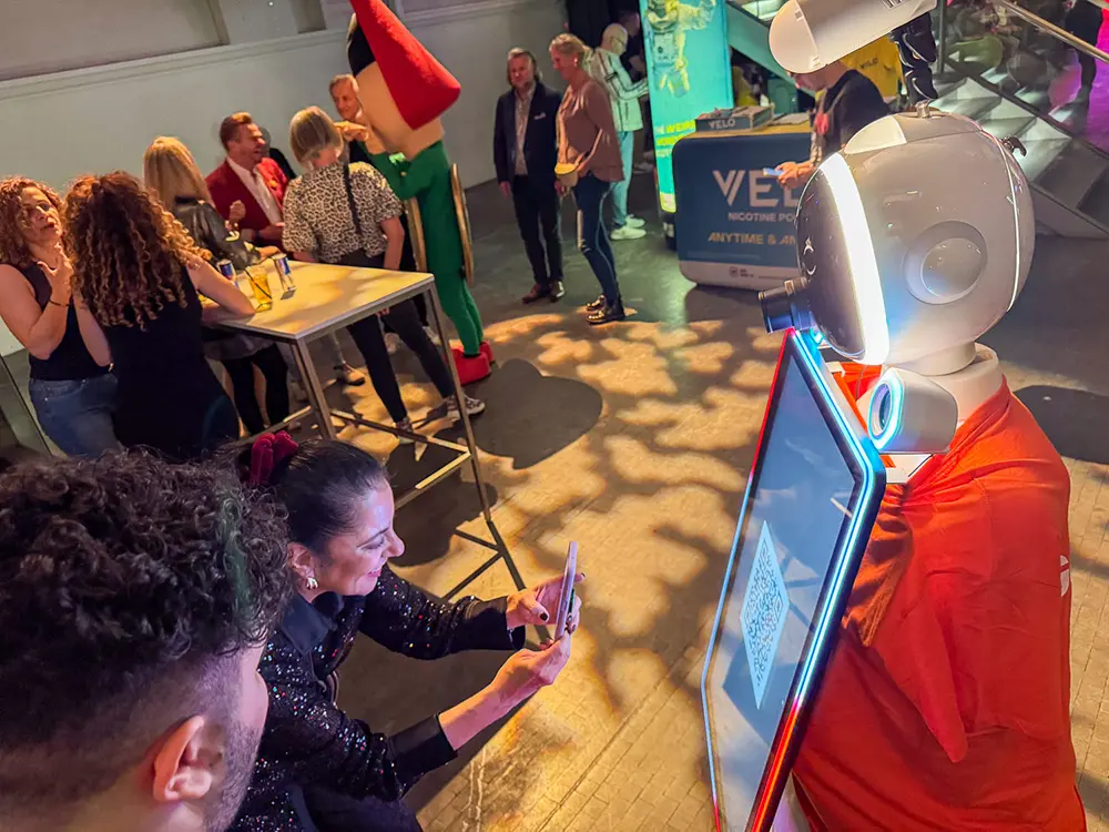 Gast fotografiert den AI Fotobox Roboter LUNA mit dem Handy bei einer Feier