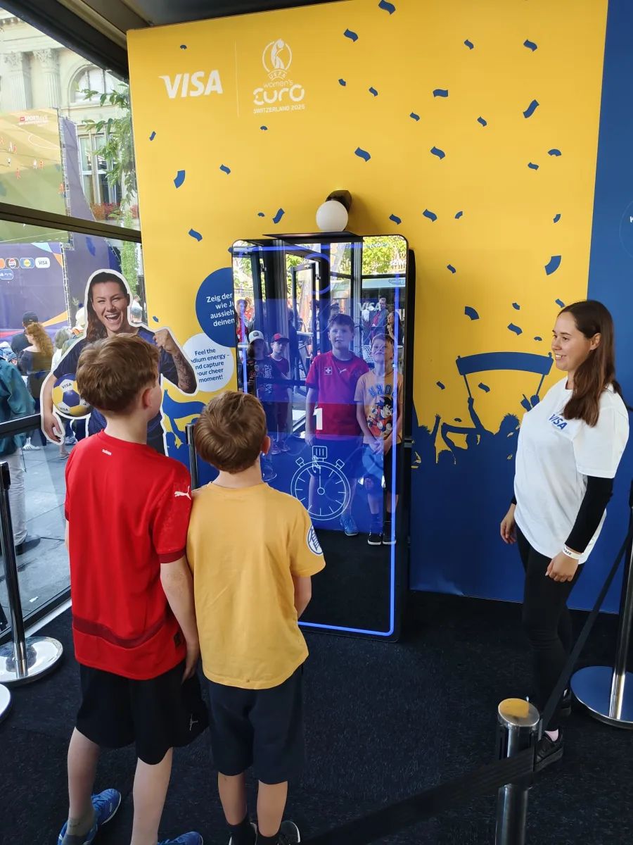 Zwei Jugendliche vor dem AI Magic Tower an einem gebrandeten Messestand