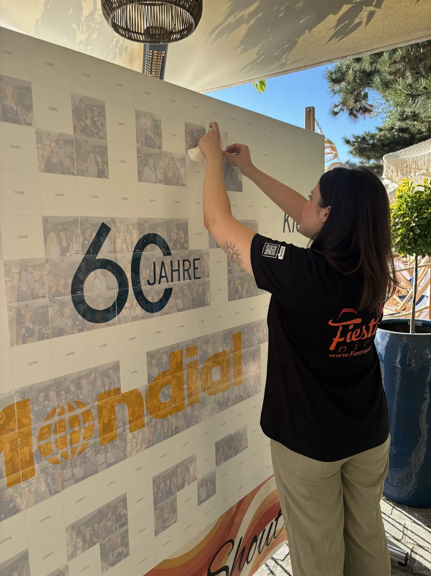 FiestaPics-Mitarbeiterin klebt ein Foto auf die fast fertige Foto-Mosaik-Wand "60 Jahre Mondial" am Wiener Donaukanal