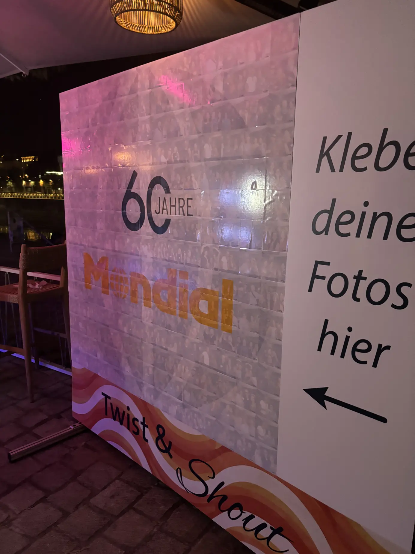Die fertige Foto-Mosaik-Wand "60 Jahre Mondial" bei Nacht, beleuchtet von bunten Partylichtern