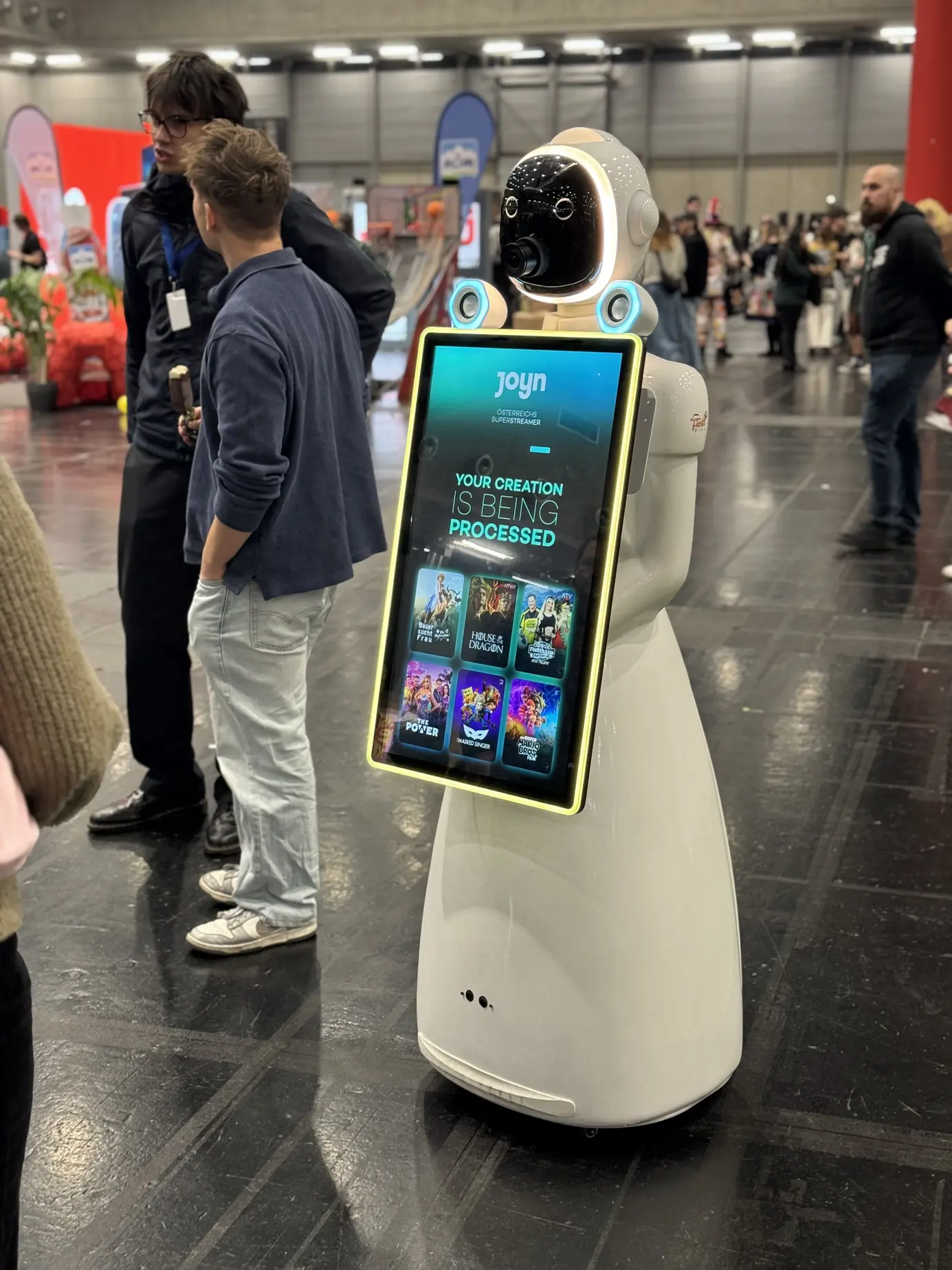 Besucher schauen auf den Joyn-gebrandeten Touchscreen des AI Fotobox Roboters LUNA