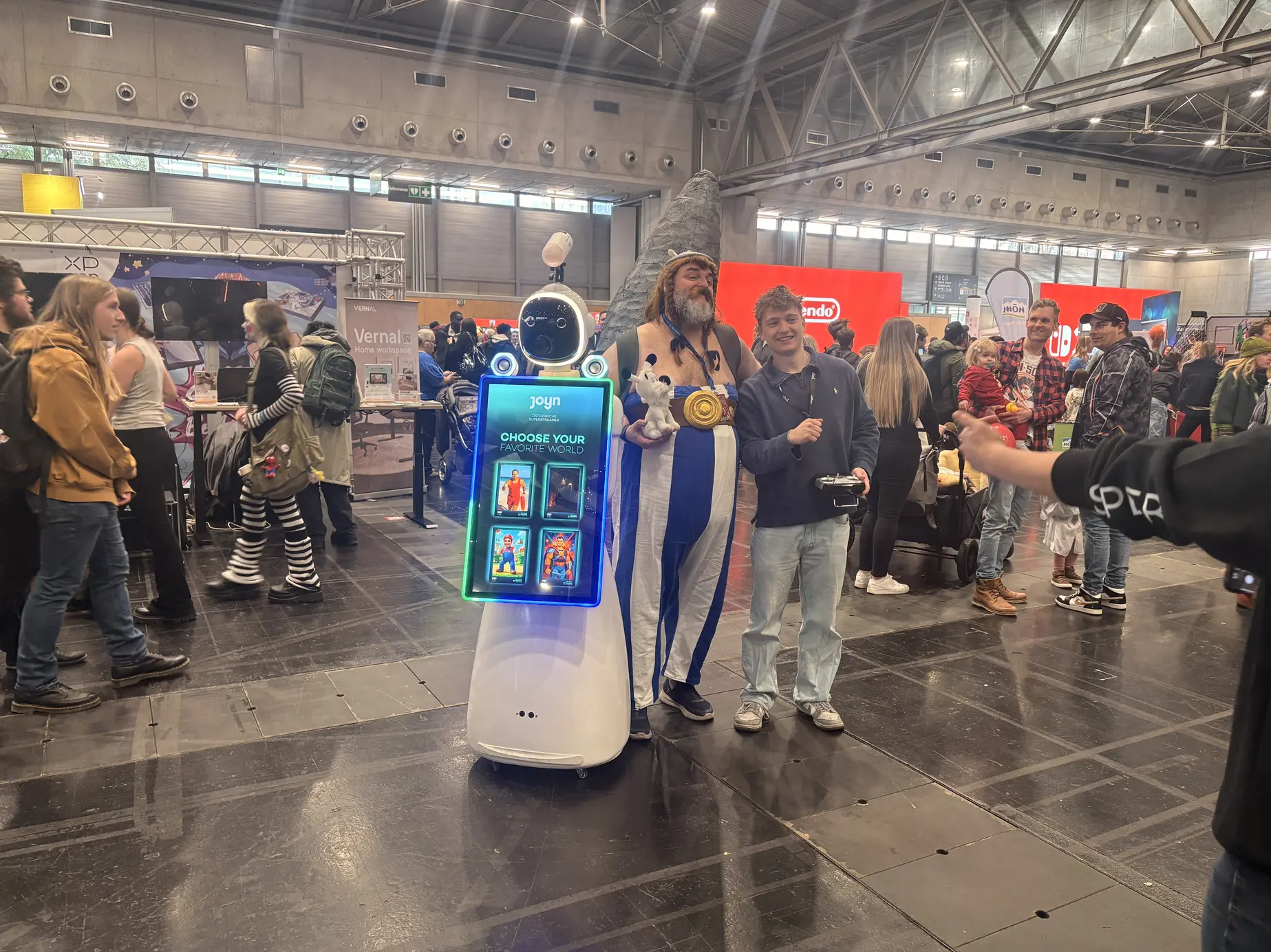Besucher und Cosplayer posieren mit dem AI Fotobox Roboter LUNA in der Messe Wien
