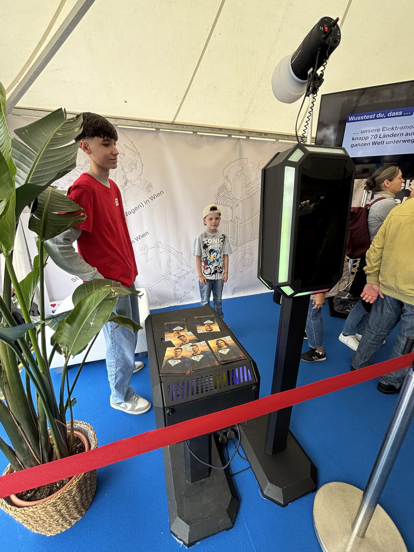 Betreuer und Gäste an der KI Fotobox im TSA-Zelt, daneben der Ständer mit den Prints