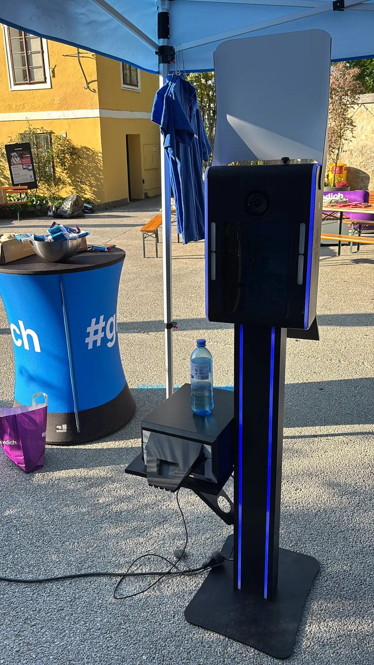 KI Fotobox mit blau leuchtender Säule, Reflektor und Druckerstand neben einem #glaubandich-Stehtisch