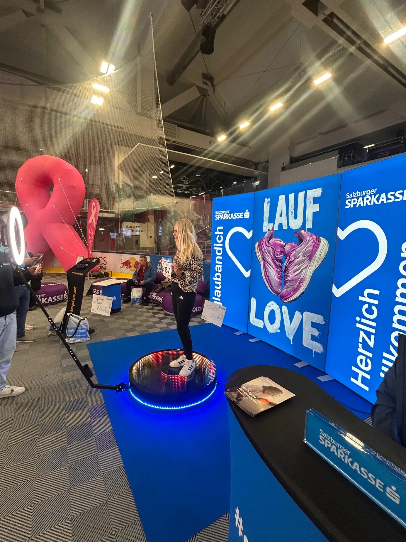 Läuferin auf der leuchtenden Plattform des 360° Ground Spinners vor der „Lauf Love“-Rückwand der Salzburger Sparkasse in der Eisarena Salzburg