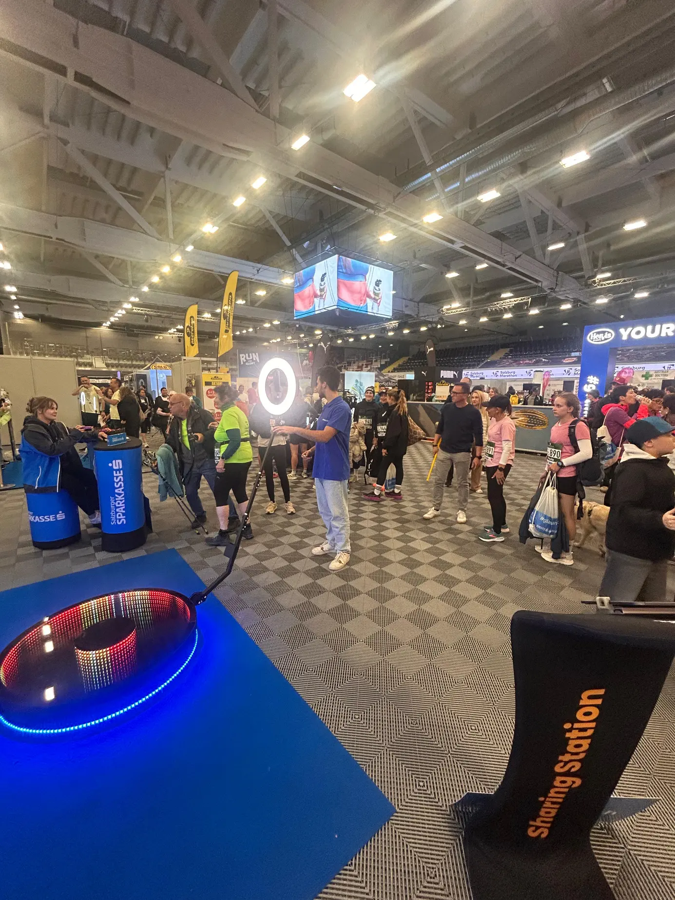 Blick über die LED-Plattform des 360° Ground Spinners und die Sharing Station in die Messehalle der SportMall mit Läuferinnen und Läufern