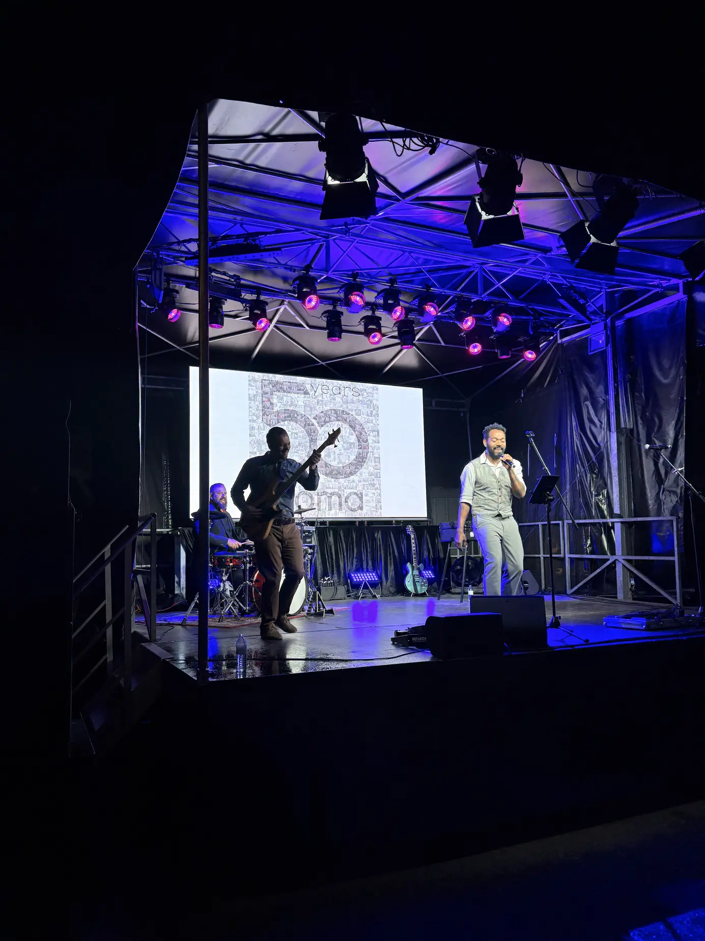 Band auf der blau beleuchteten Bühne, dahinter die LED-Wall mit dem Live-Mosaik aus Gästefotos in Form des Logos 50 years croma