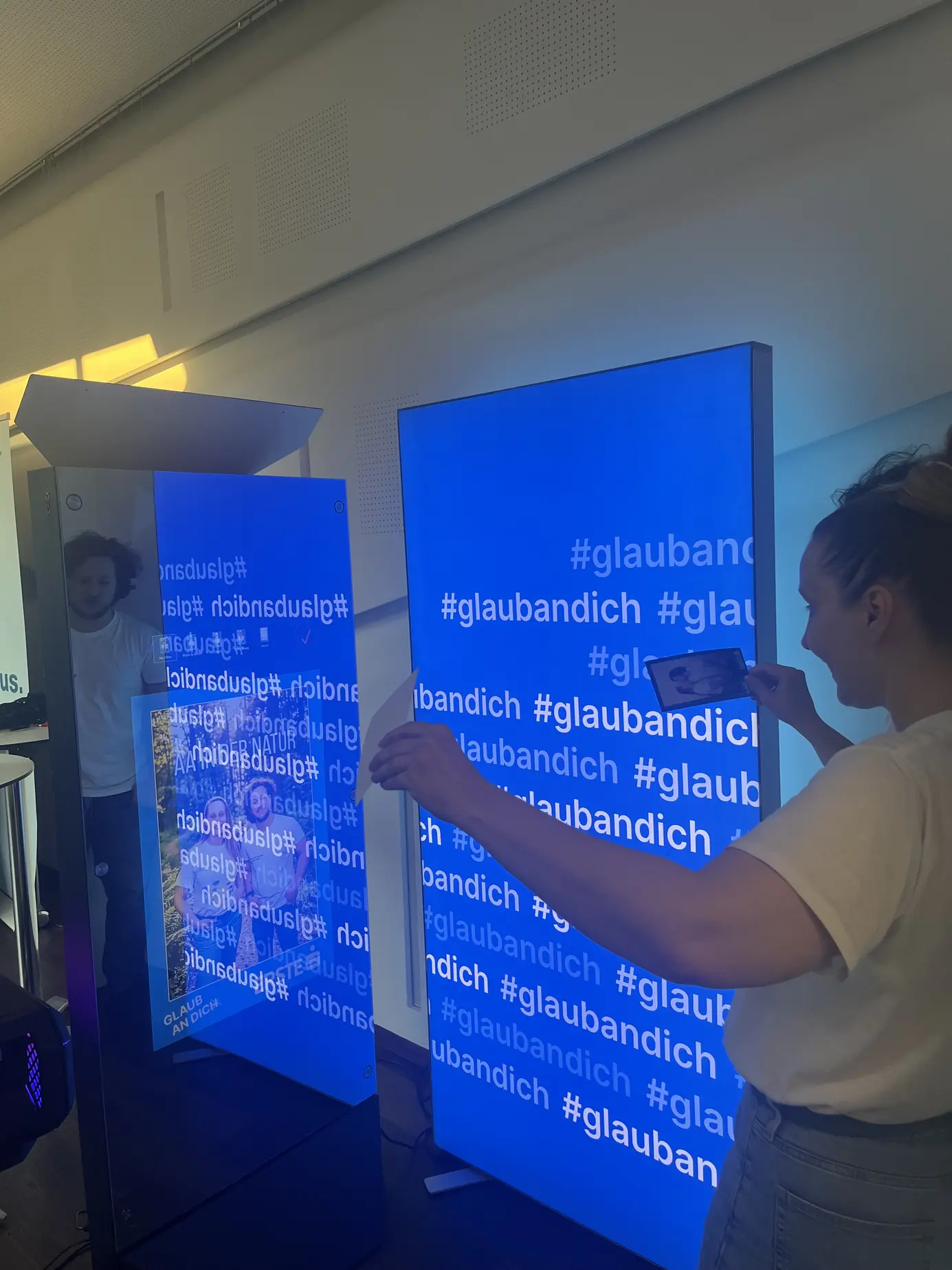 Eine Besucherin fotografiert bei TEDxDonauinsel im MuTh ihr KI-Bild direkt vom AI Magic Mirror, daneben die #glaubandich-Wand der Erste Bank