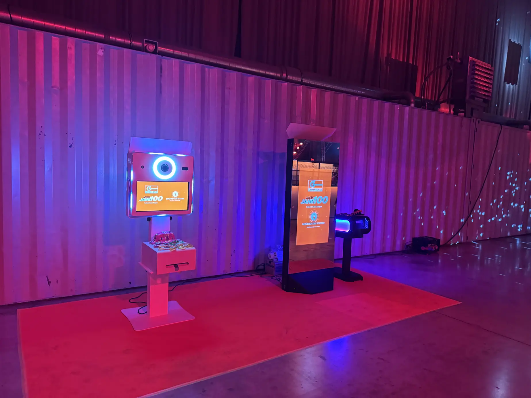 Fotobox Classic und Magic Mirror X in rot-violettem Hallenlicht vor der Wellblechwand der Marx Halle
