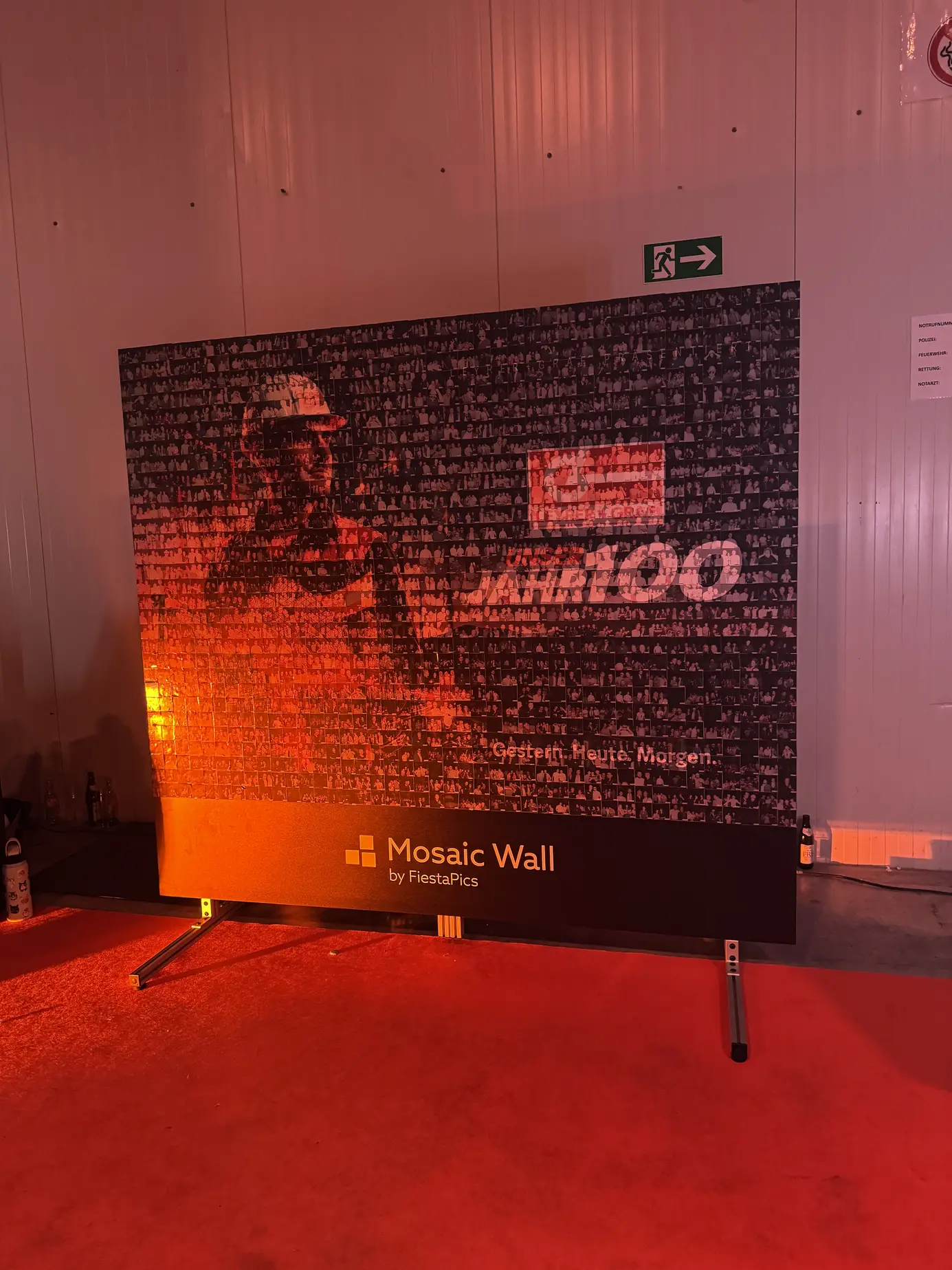 Fertig geklebte Photo Mosaic Wall mit Jubiläumsmotiv und Schriftzug 100 Jahre, angestrahlt in Orange