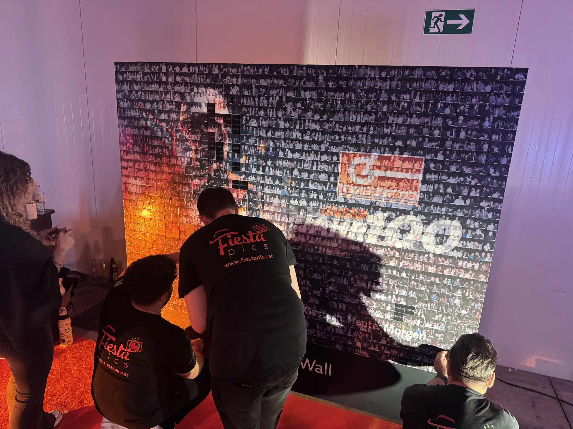 FiestaPics-Team und Gäste kleben Fotosticker an die fast fertige Photo Mosaic Wall zum 100-Jahr-Jubiläum von Leyrer + Graf in der Marx Halle