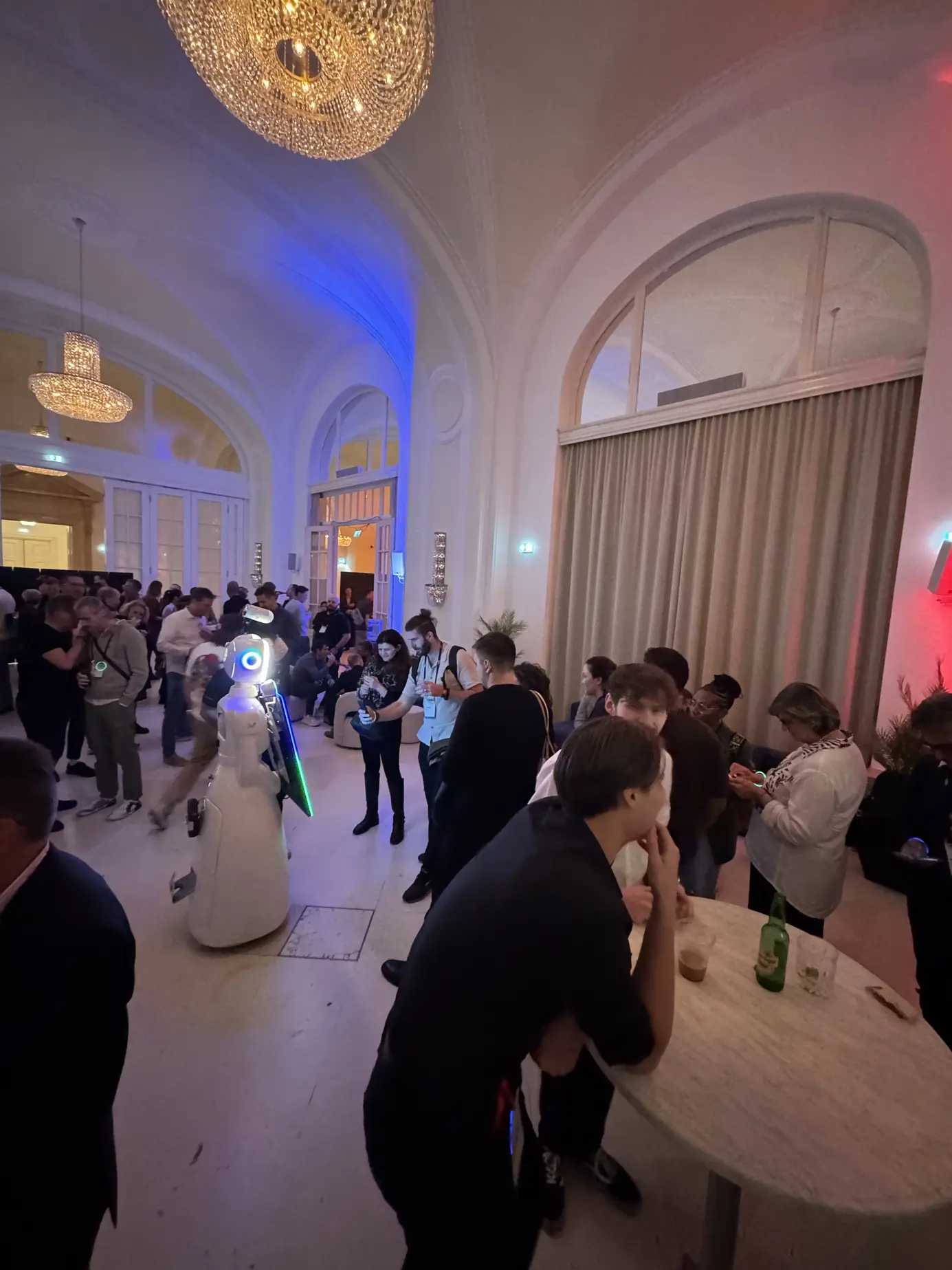 Volle Lounge der TEDAI Vienna 2025 unter Kristalllustern, mittendrin der leuchtende KI-Roboter LUNA