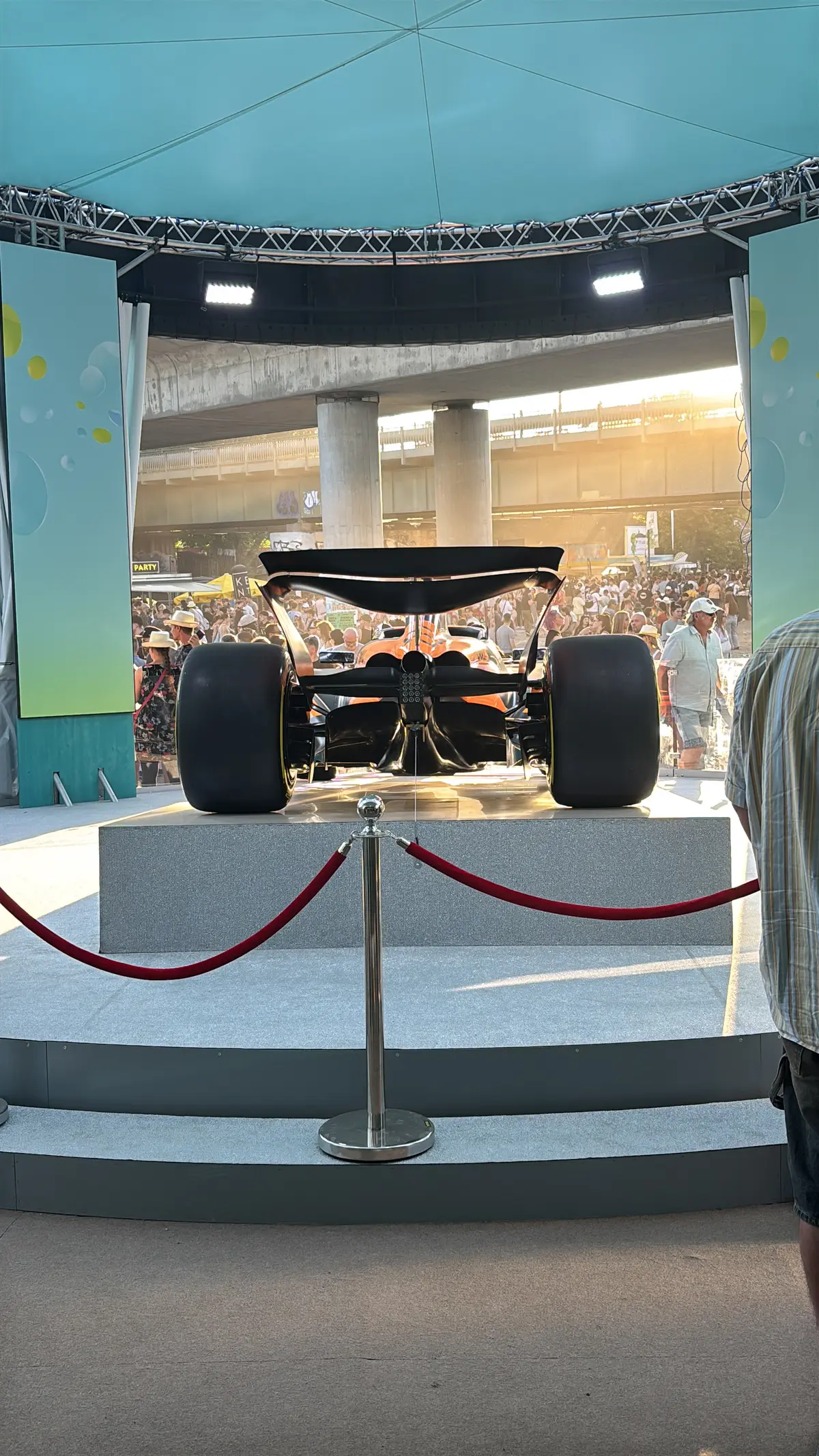 Formel-1-Showcar auf einem Podest hinter roter Absperrkordel am Donauinselfest 2025, dahinter Festivalbesucher
