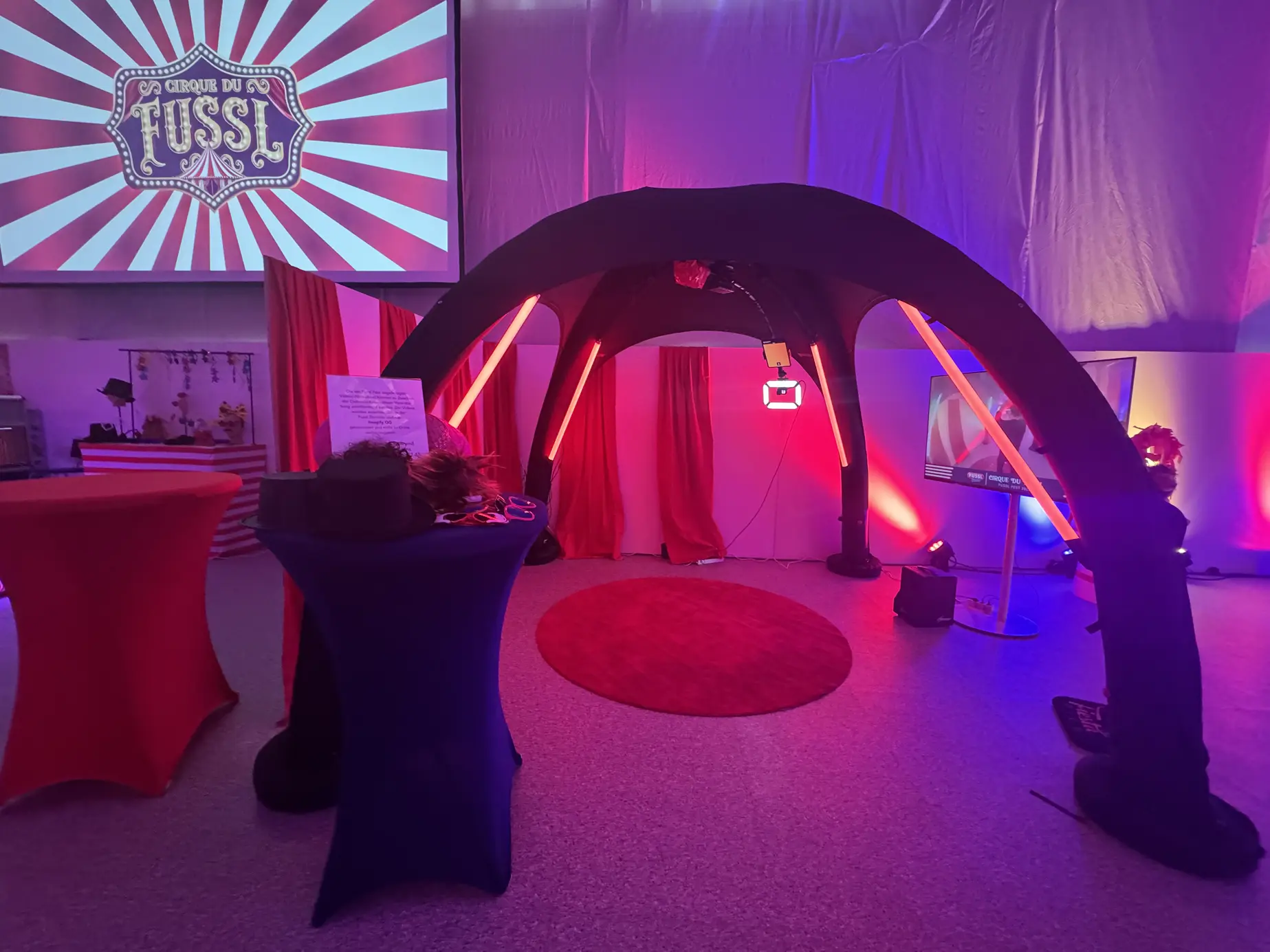 360° Headspinner unter schwarzem LED-Bogen mit rotem Manegen-Teppich, im Hintergrund die Leinwand mit dem Cirque du Fussl Logo