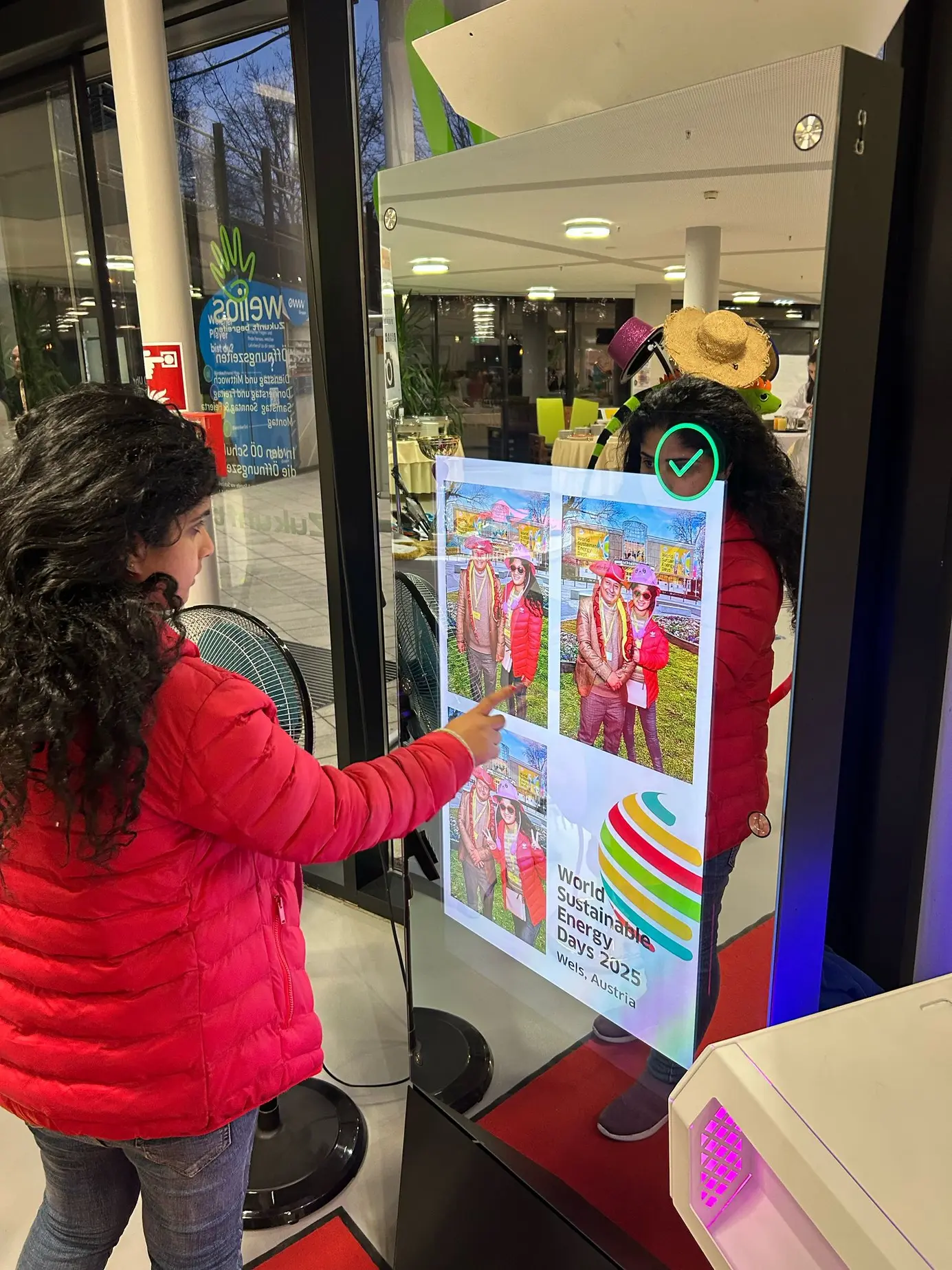 Nahaufnahme des Magic Mirror X mit Fotostreifen im Design der World Sustainable Energy Days 2025 und Messegebäude als virtuellem Hintergrund