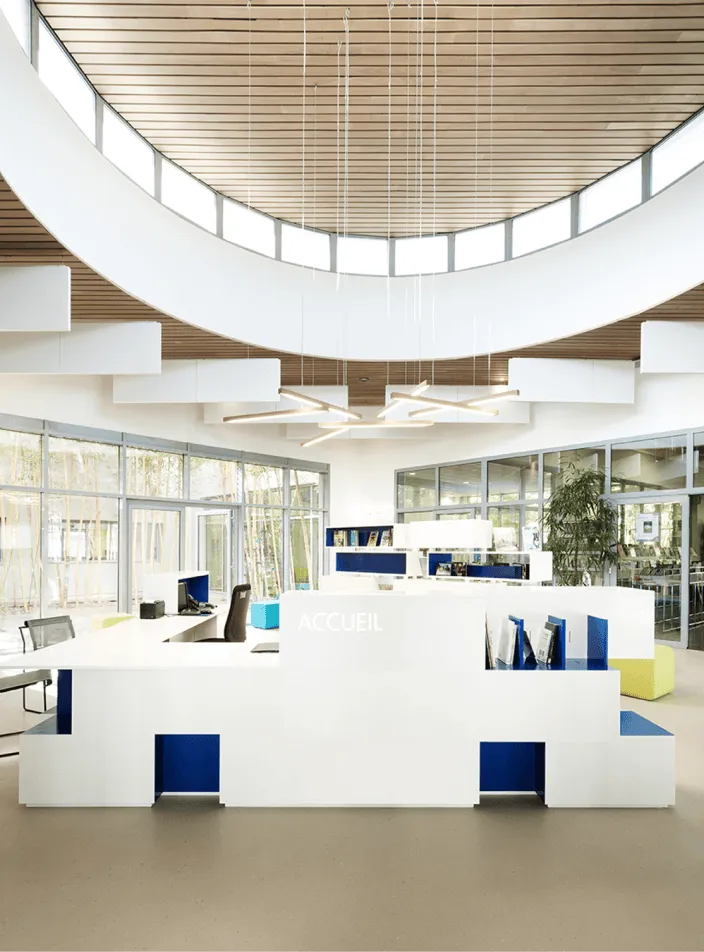 Ouvrage de menuiserie bois sur mesure : hall d'accueil lumineux au comptoir blanc rehaussé de bleu et plafond circulaire en lattes de bois.