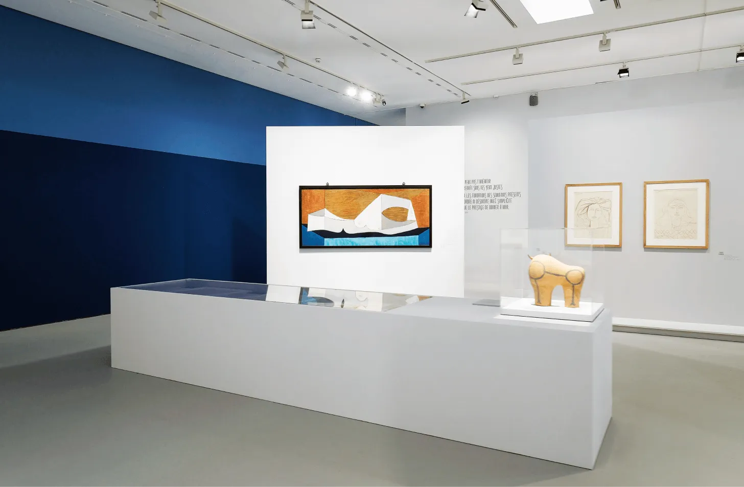 Menuiserie d'agencement sur mesure : salle d'exposition épurée au socle blanc, sculpture et tableau coloré sur mur blanc, cimaise bleu profond.