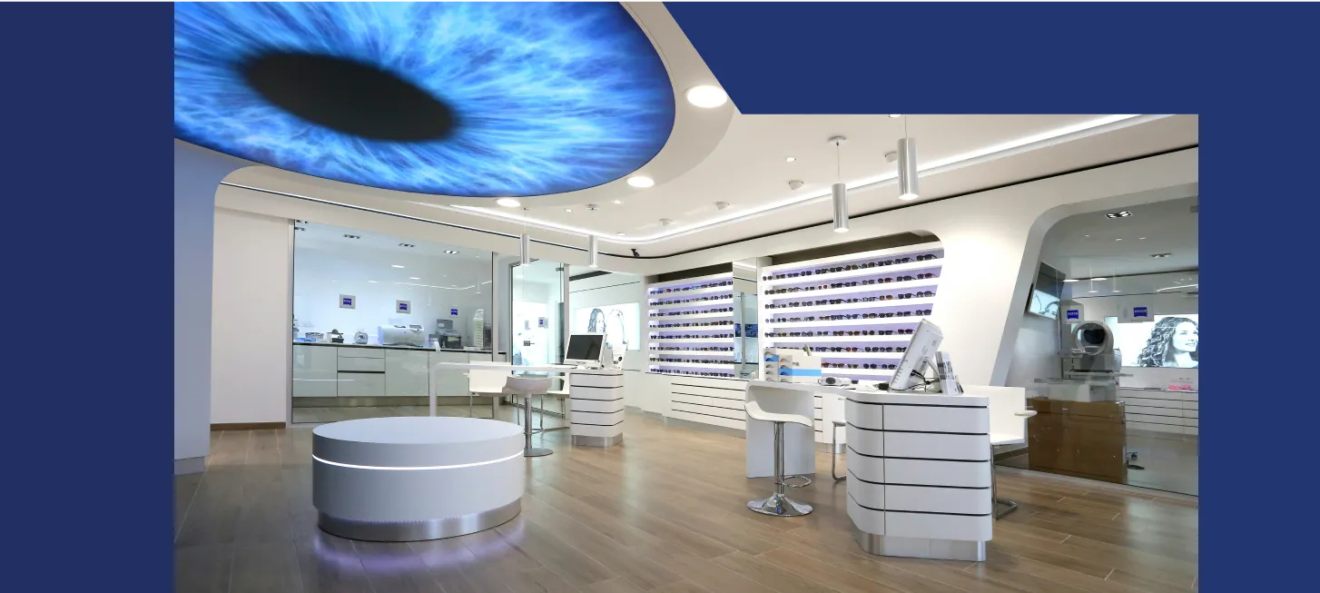 Agencement de magasin d'optique en menuiserie sur mesure : intérieur moderne au plafond lumineux en forme d'œil bleu, présentoirs blancs de lunettes et sol en bois, par un menuisier agenceur à Mauguio.
