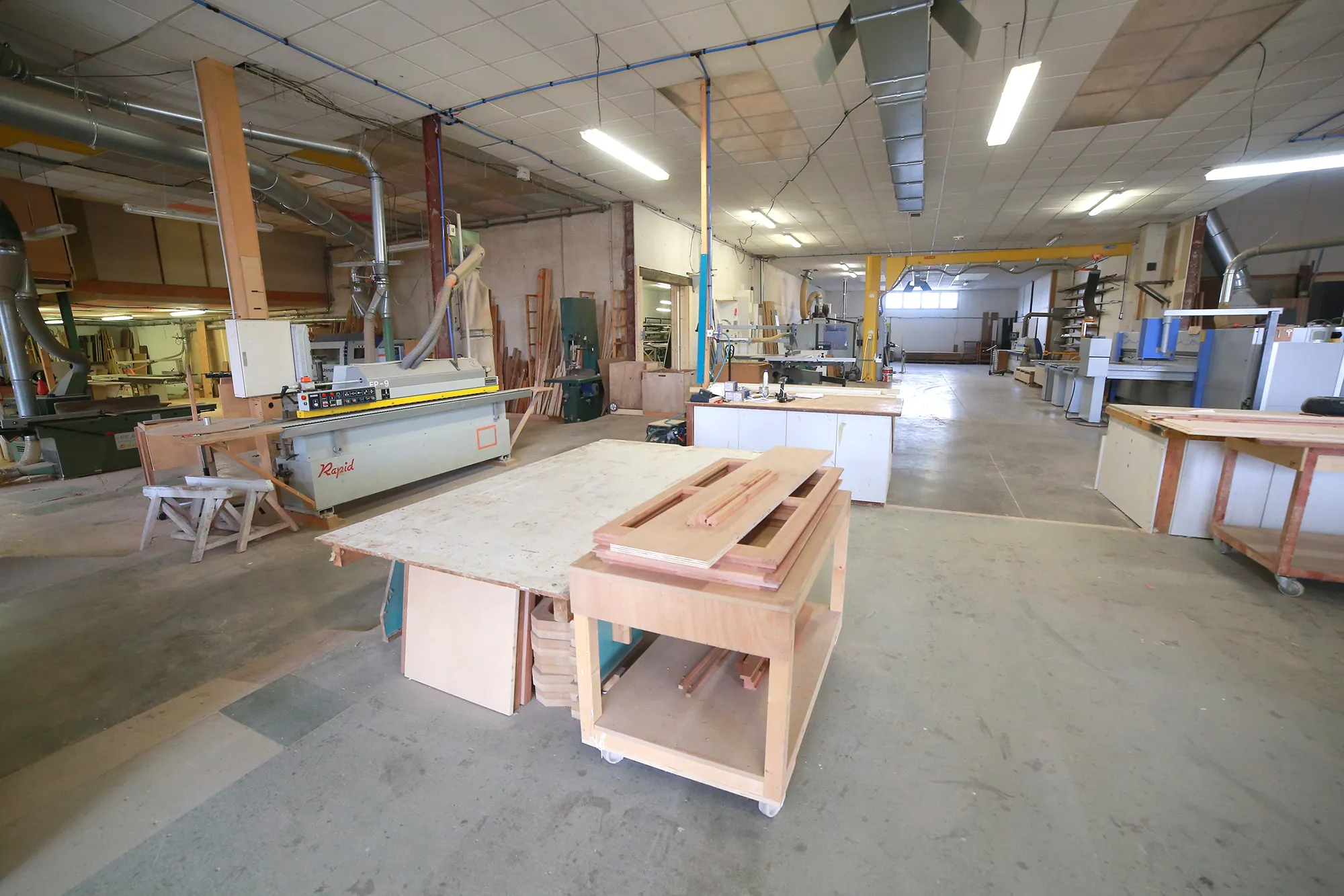 Atelier de menuiserie : établi mobile, panneaux de bois, machines et système d'aspiration sous charpente métallique, équipement d'un atelier de menuiserie à Montpellier