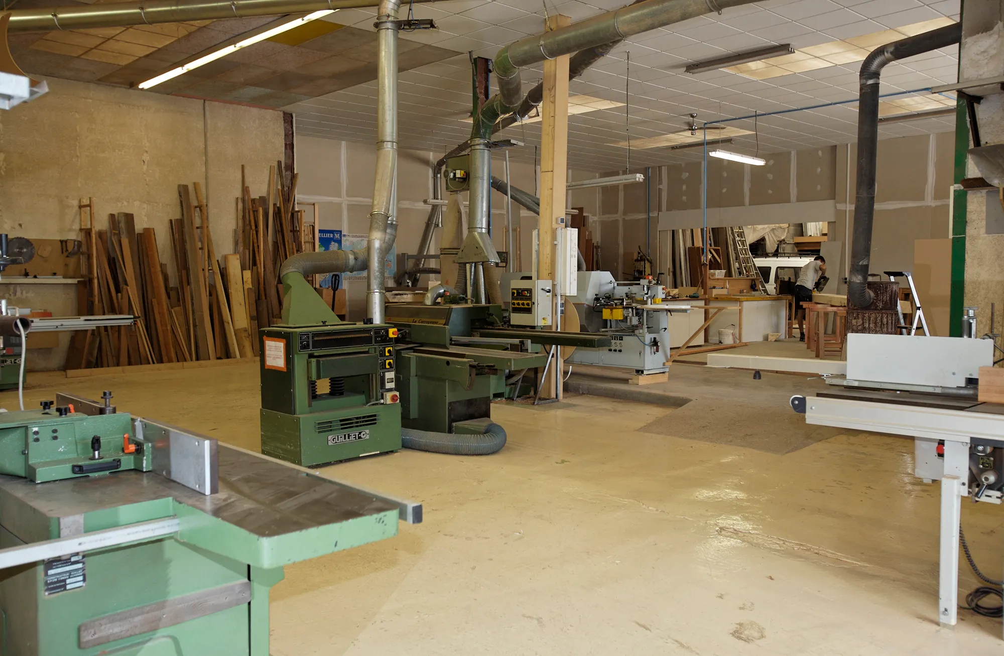 Fabrication sur mesure en atelier de menuiserie : machines à bois vertes, stocks de planches, aspiration et établis, atelier de menuiserie de Lunel