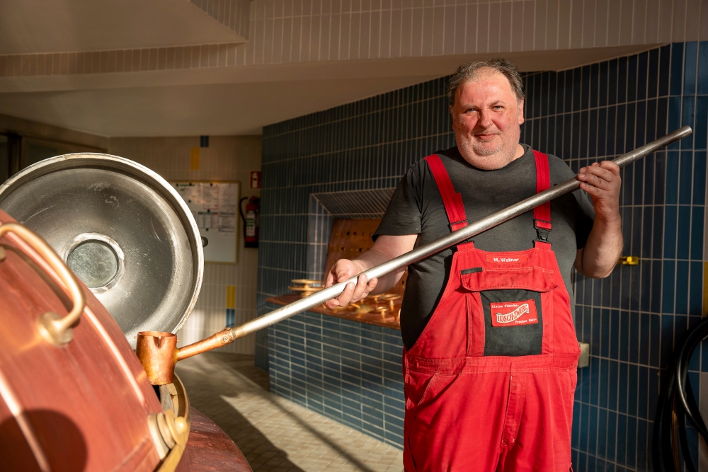Ein Mann in roter Latzhose schöpft etwas aus einem Kessel