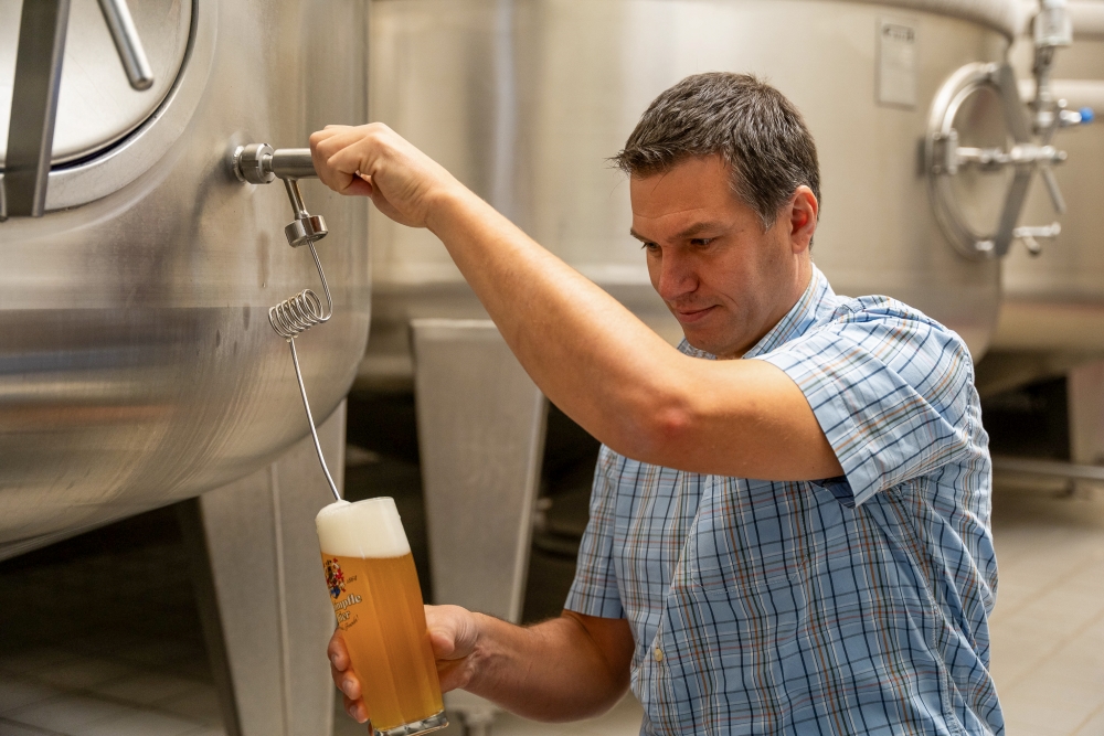 Ein Mann im karierten Hemd zapft Bier aus einer Maschine in der Brauerei.