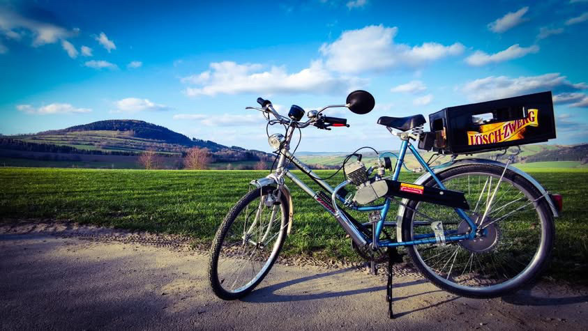 Ein Fahrrad steht am Wegrand, auf dem Gepäckträger ist eine Kiste Lösch-Zwerg.