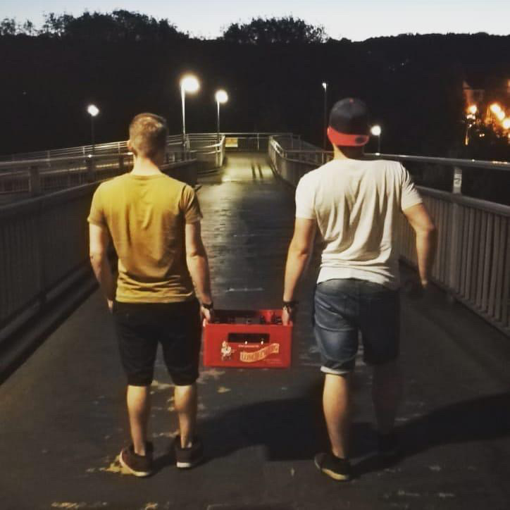 Zwei Männer laufen eine Straße entlang und tragen eine Lösch-Zwerg-Kiste.