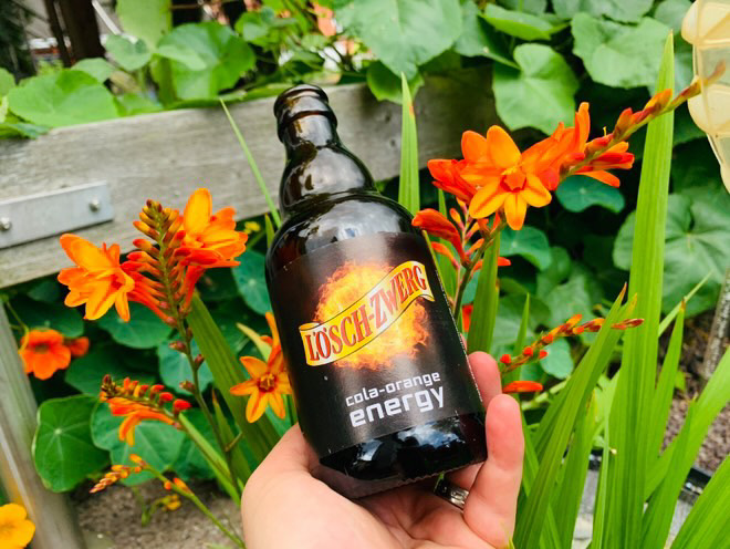 Jemand hält eine Lösch-Zwerg-Flasche vor Blumen.