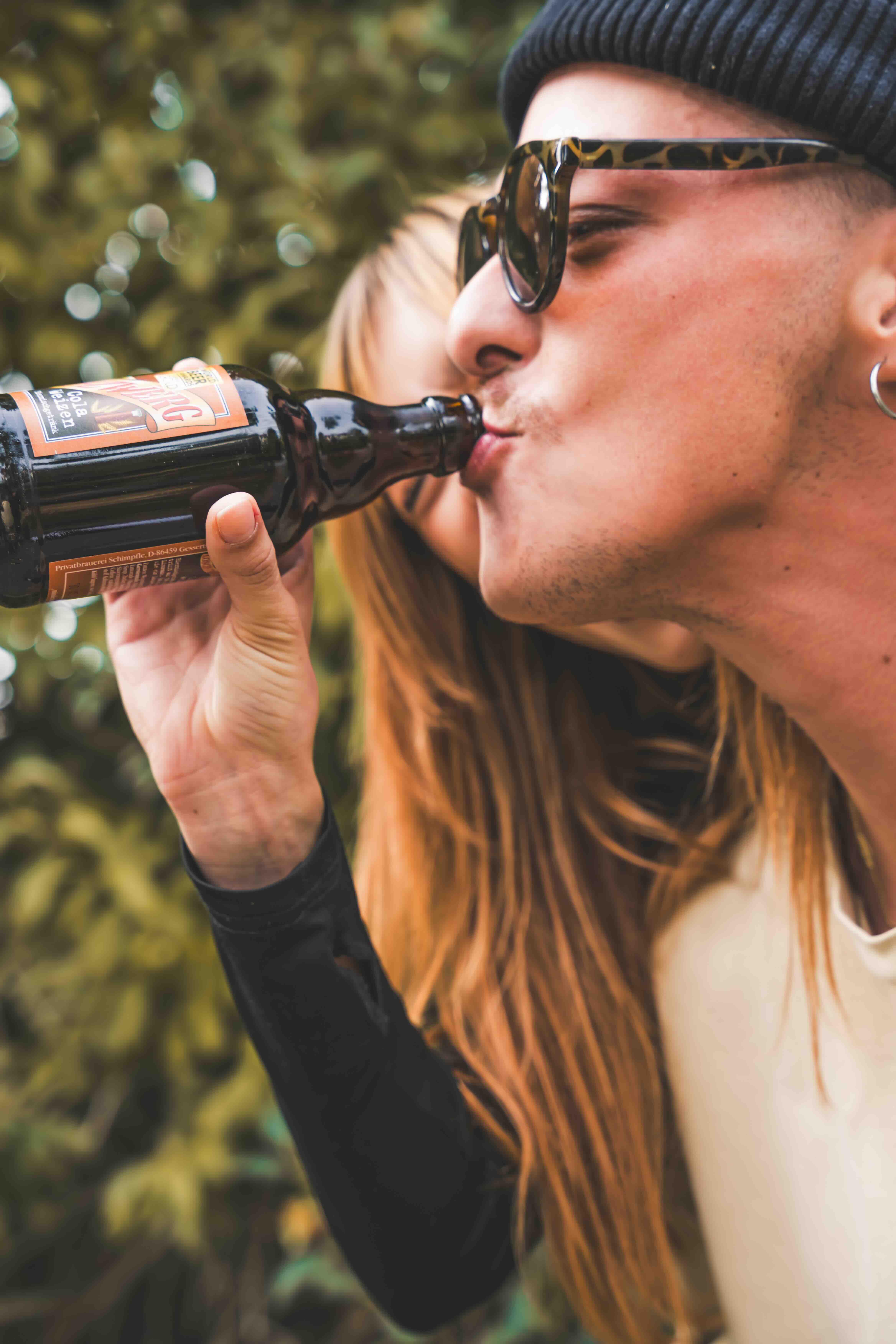 Eine Frau hält eine Flasche, sodass ein Mann daraus trinken kann.
