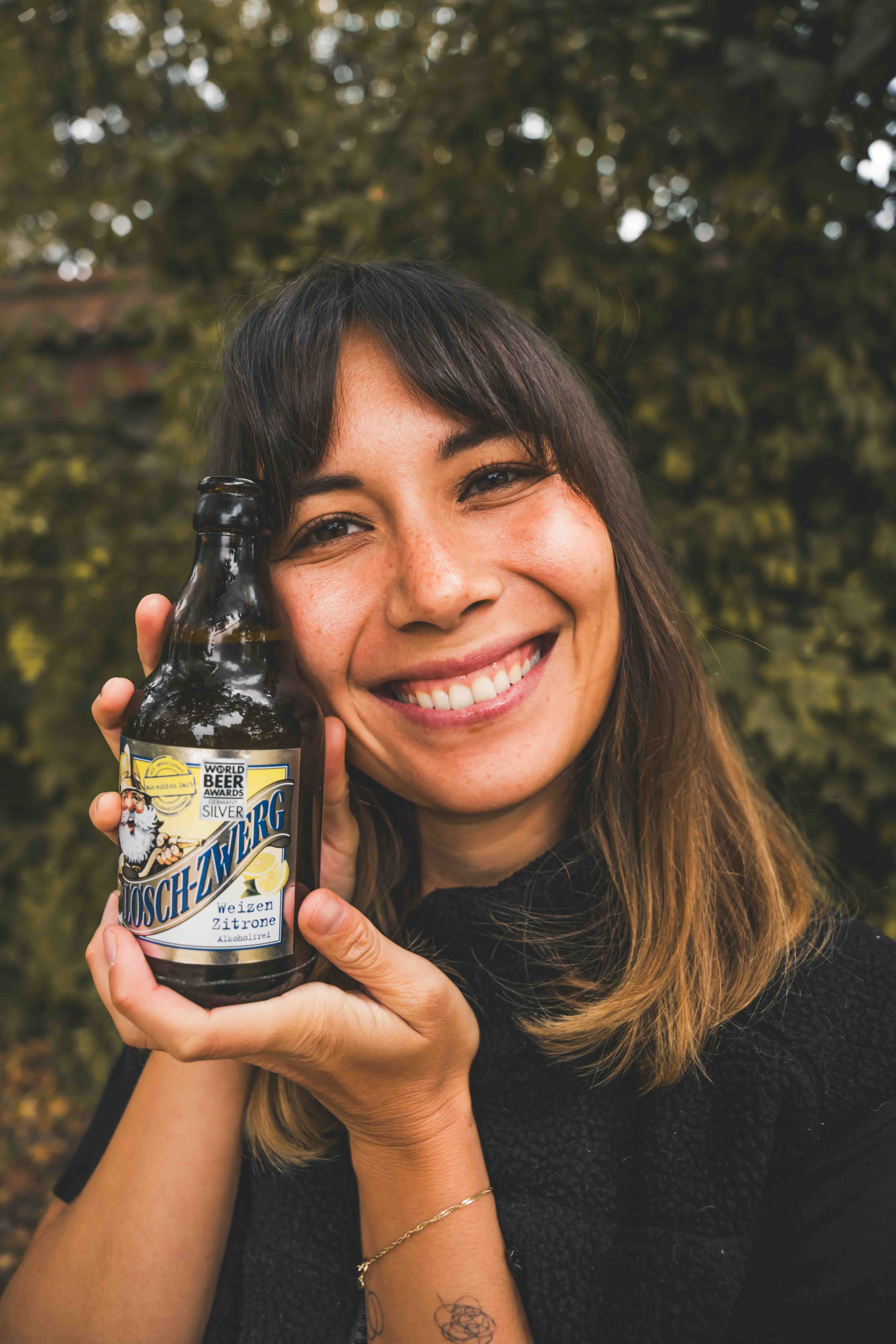 Eine Frau posiert lächelnd mit einer Lösch-Zwerg-Flasche