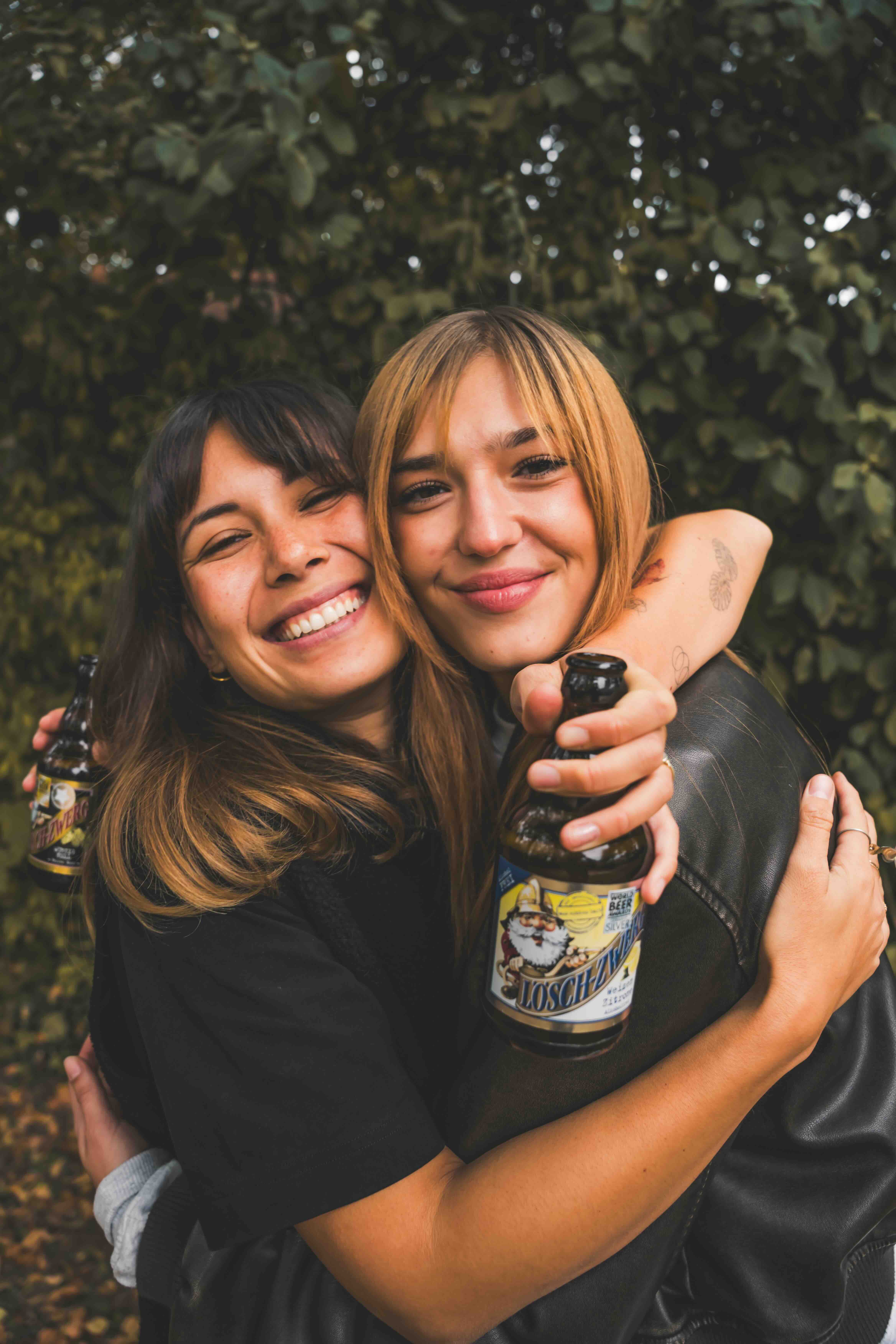 Zwei Frauen umarmen sich. Eine hält eine Lösch-Zwerg-Flasche.