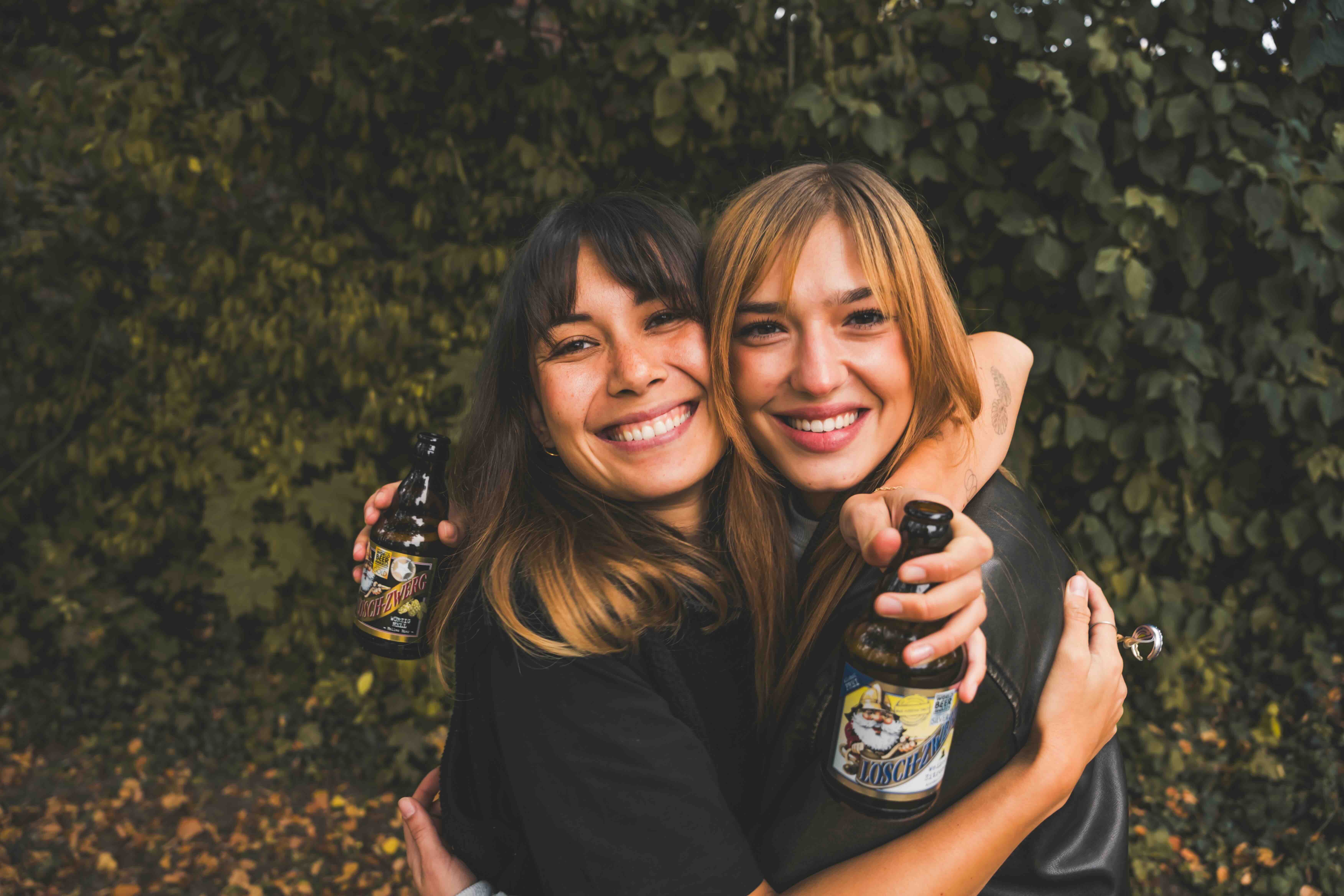 Zwei Frauen umarmen sich. Eine hält eine Lösch-Zwerg-Flasche.