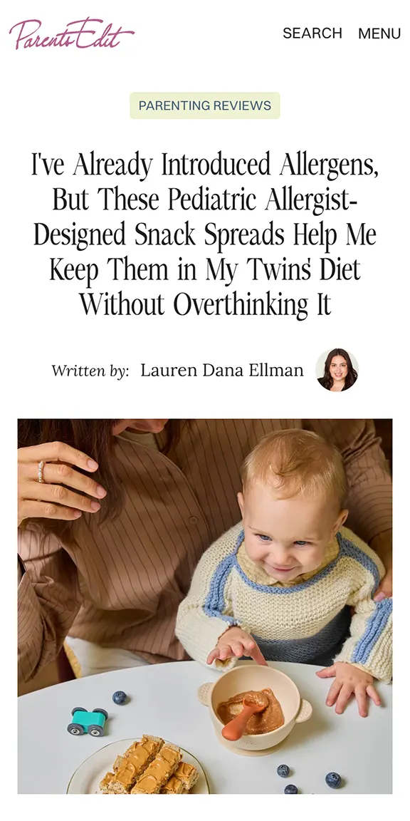 Young child in knit sweater reaching for peanut butter snack at a table with blueberries and toy car.