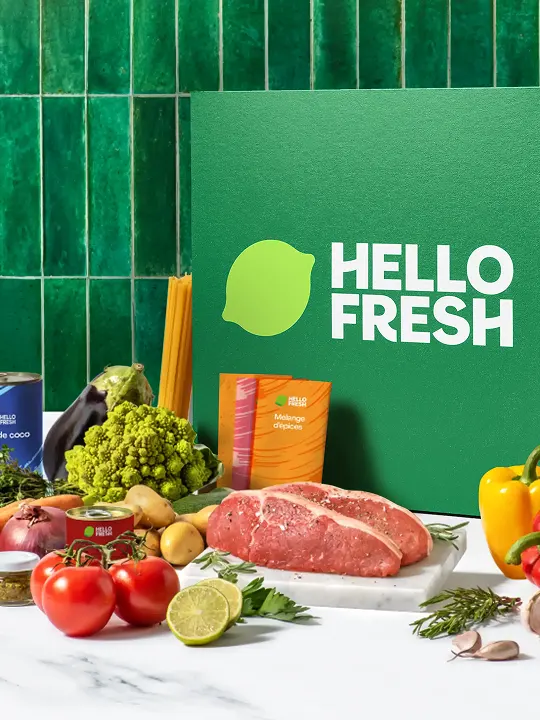 HelloFresh green box with fresh vegetables, raw meat, and spice packets on a white countertop.