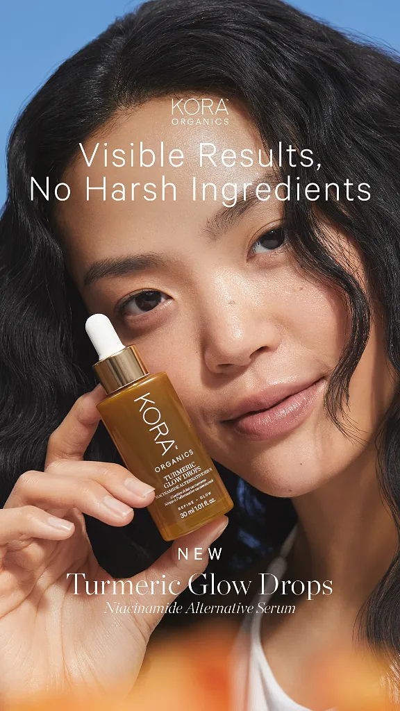 Woman with glowing skin holds Kora Organics Turmeric Glow Drops serum bottle.