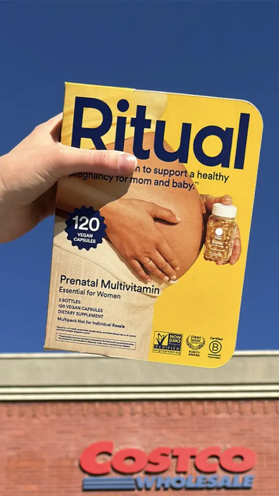 Hand holding Ritual Prenatal Multivitamin box for women against blue sky with Costco Wholesale sign below.