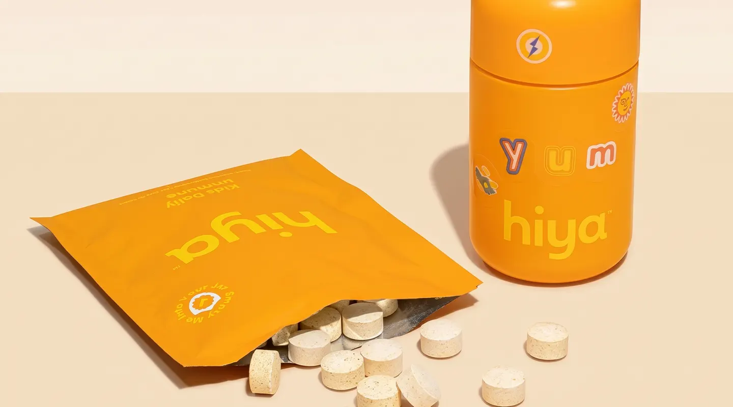 Orange Hiya supplement package and bottle with scattered round tablets on beige surface.