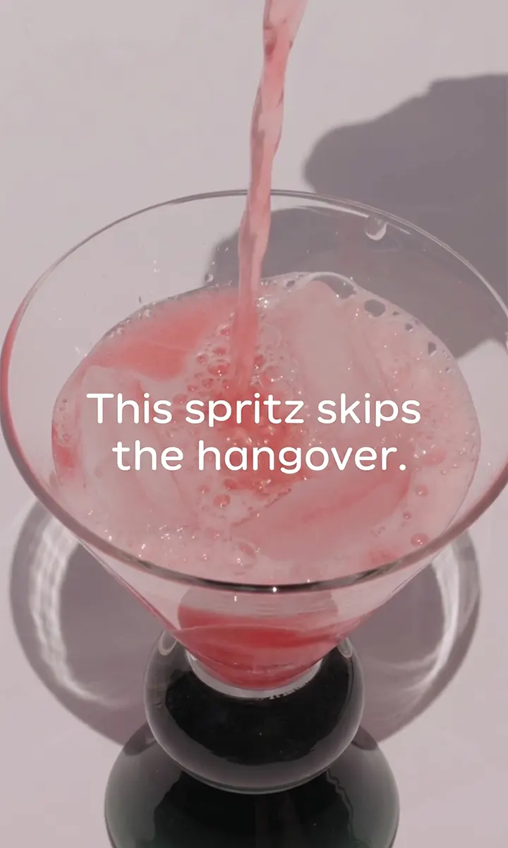 Pink spritz drink with ice being poured into a glass with text: This spritz skips the hangover.