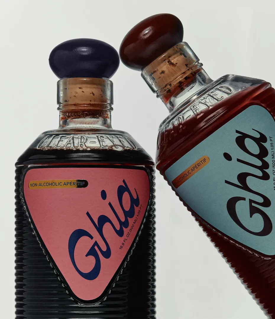 Two Ghia non-alcoholic aperitif bottles with cork stoppers, one with a pink label and one with a blue label.