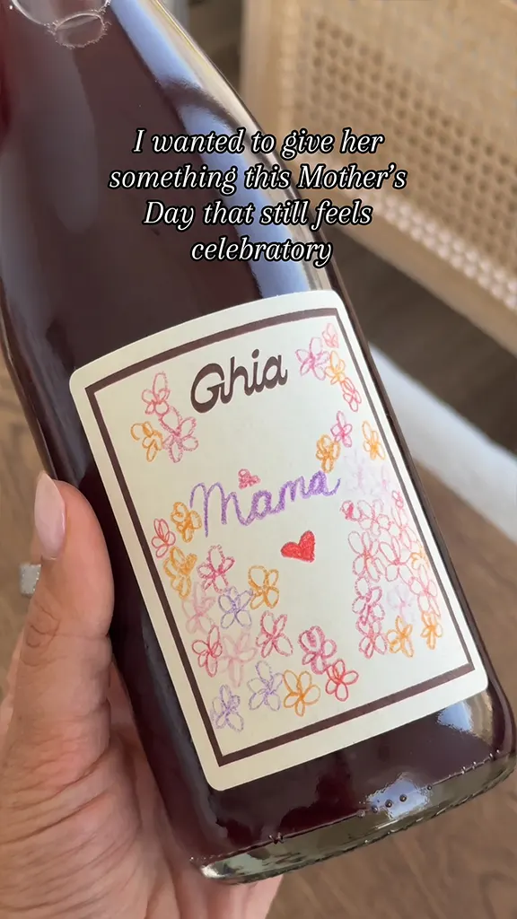 Hand holding a Ghia bottle with a Mother's Day label decorated with colorful flowers and the word Mama.