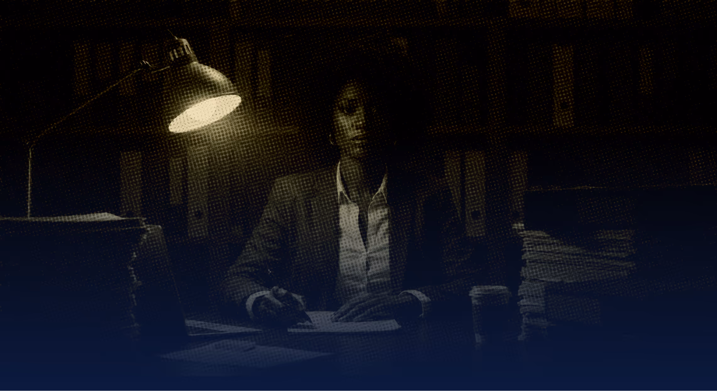 A woman sitting at a desk in front of a lamp.