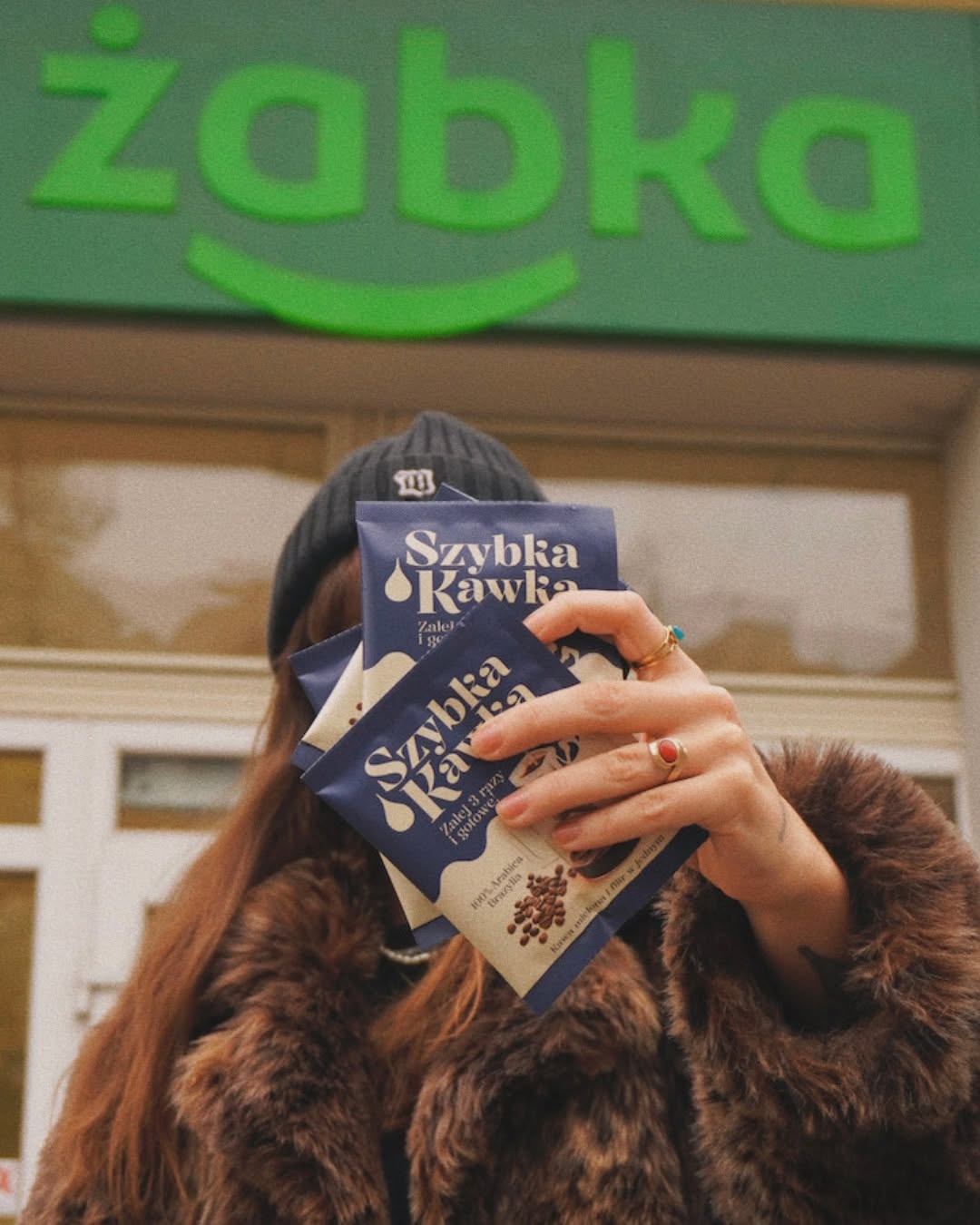 Klientka z saszetkami Szybkiej Kawki przed sklepem Żabka