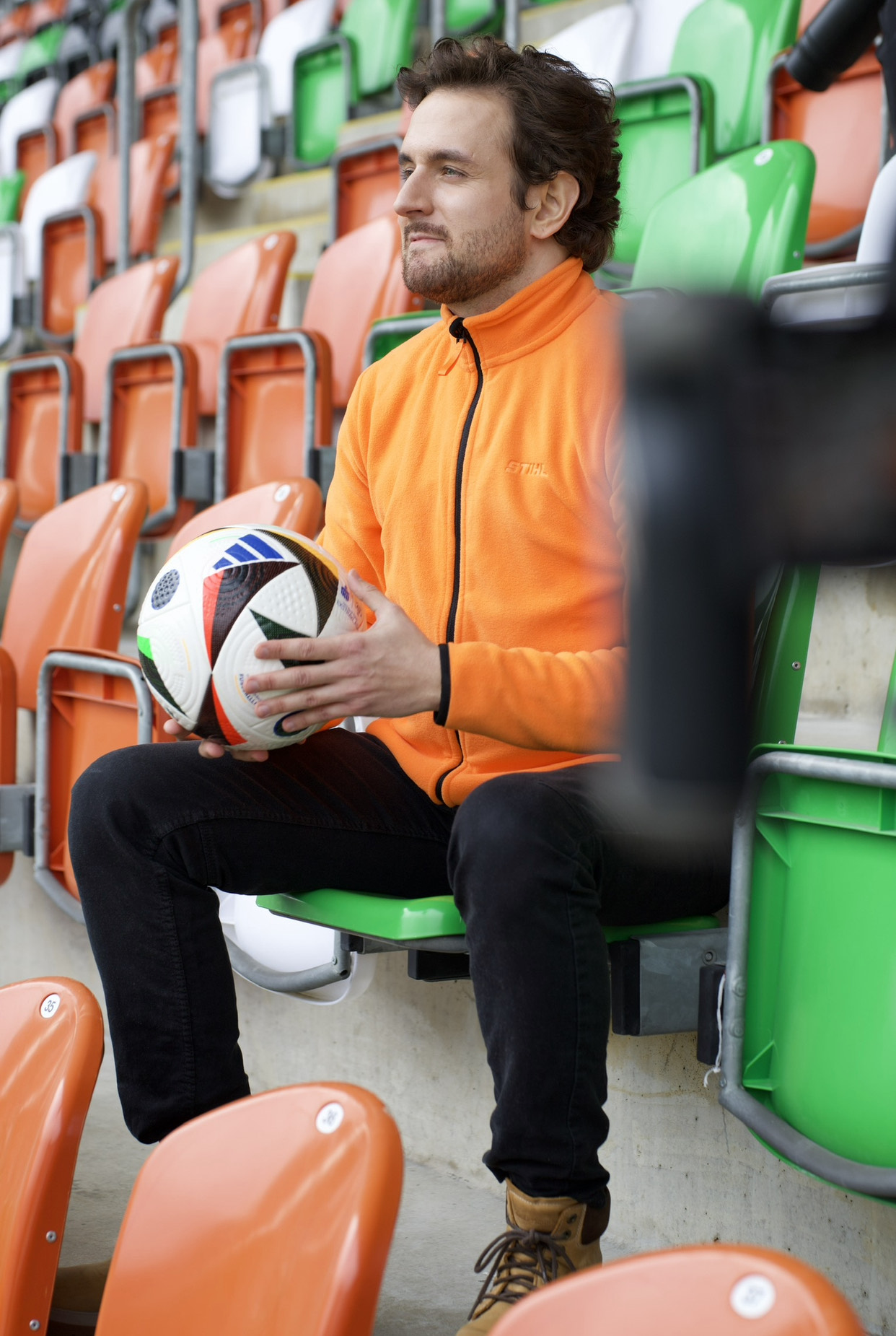 Mężczyzna w polarze STIHL z piłką na trybunie stadionu