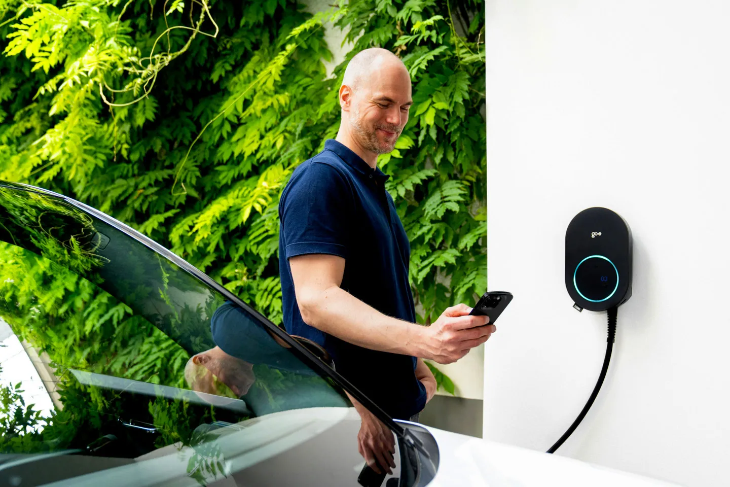 Techniker in gelbem T-Shirt montiert Solarpanels auf einem Dach vor grünem Laub im Sonnenschein.