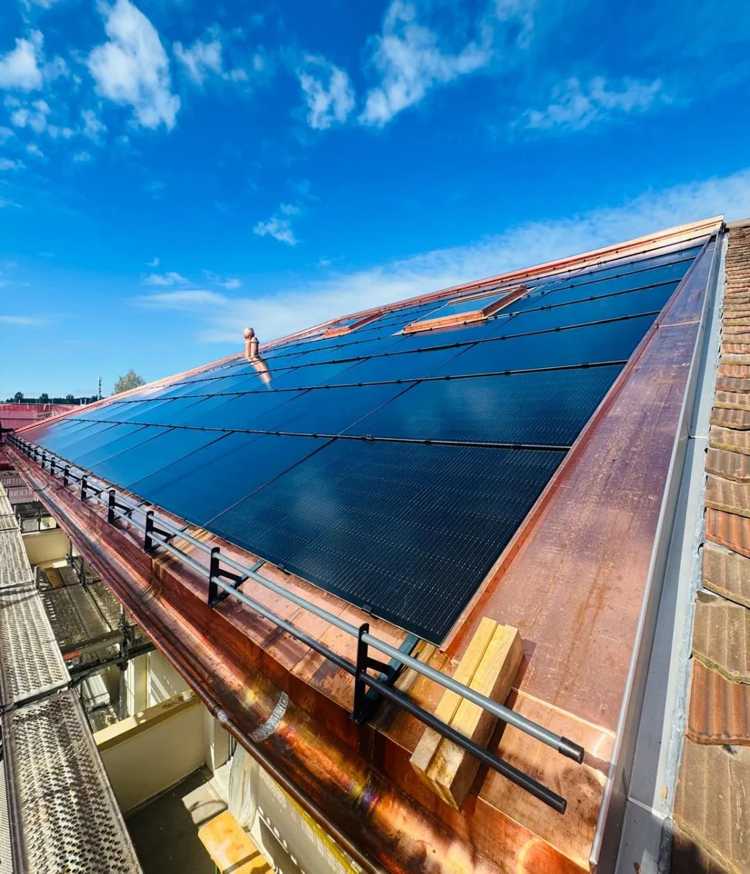 Techniker in gelbem T-Shirt montiert Solarpanels auf einem Dach vor grünem Laub im Sonnenschein.