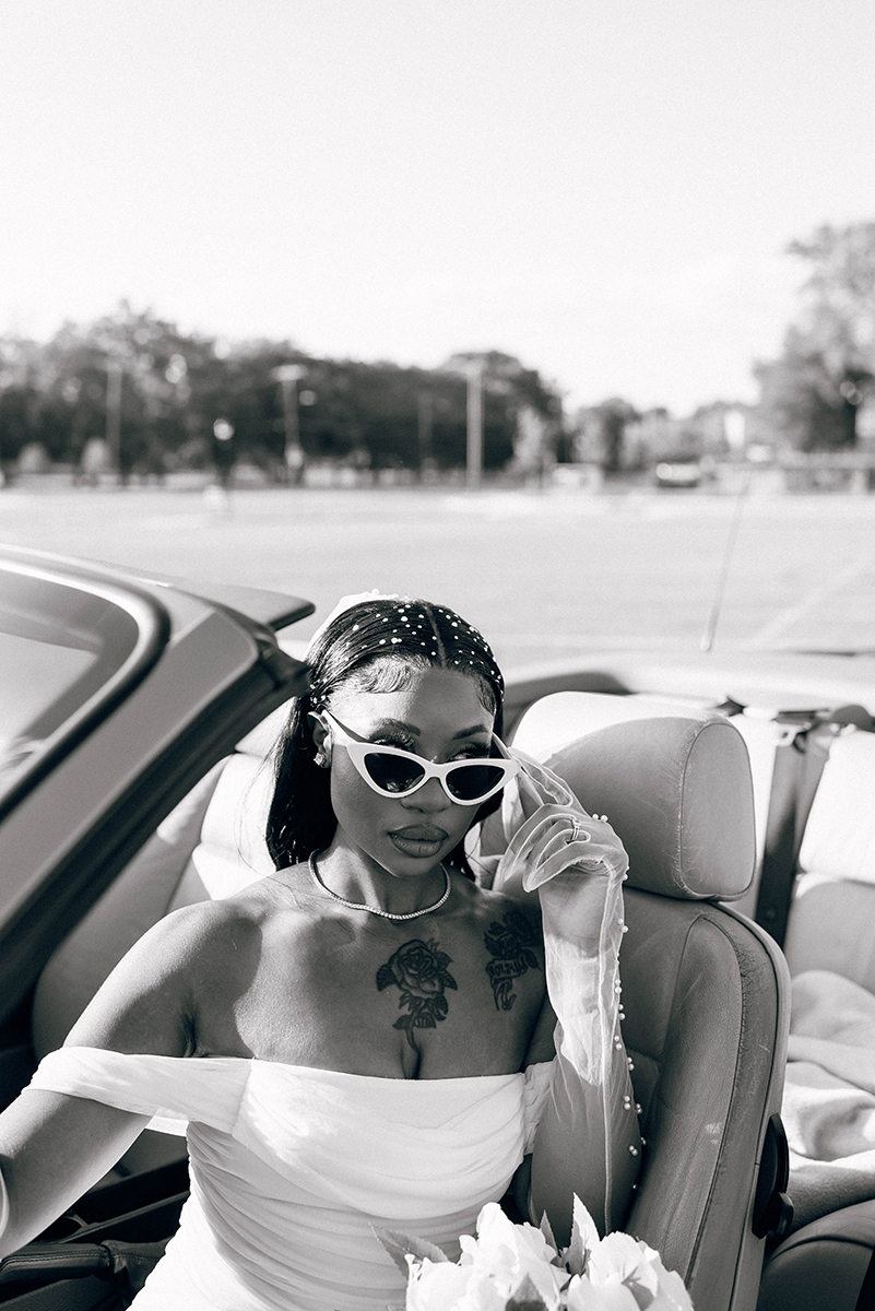 Elopement styled shoot in Camp North End Charlotte, NC with same-sex couple in classic BMW convertible. Bride in driver's seat holding sunglasses looking at camera