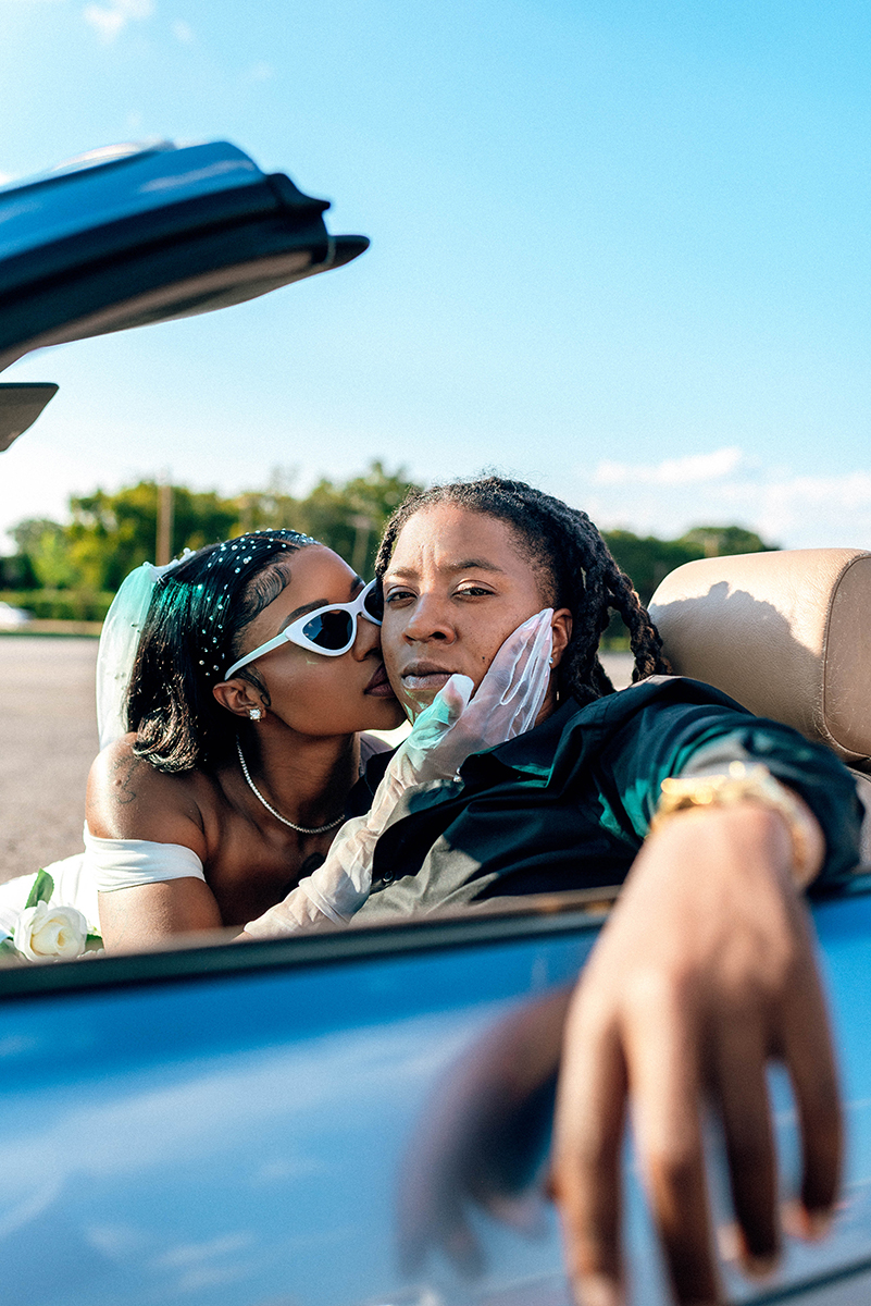 Elopement styled shoot in Camp North End Charlotte, NC with same-sex couple in classic BMW convertible. couple sitting in front seat. Bride kissing other partner on cheek while they look at camera