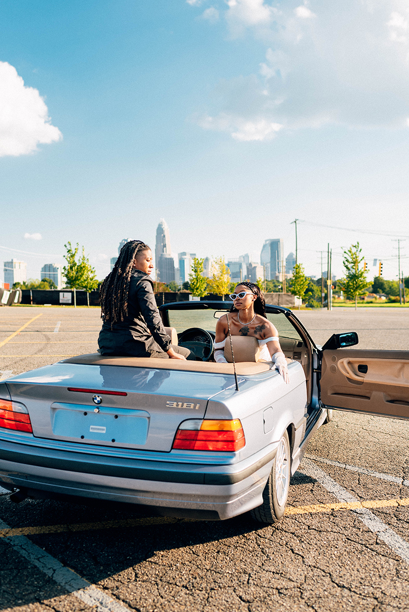 Elopement styled shoot in Camp North End Charlotte, NC with same-sex couple in classic BMW convertible. Bride in passenger seat facing backwards, other partner sitting on top of backseat trunk space